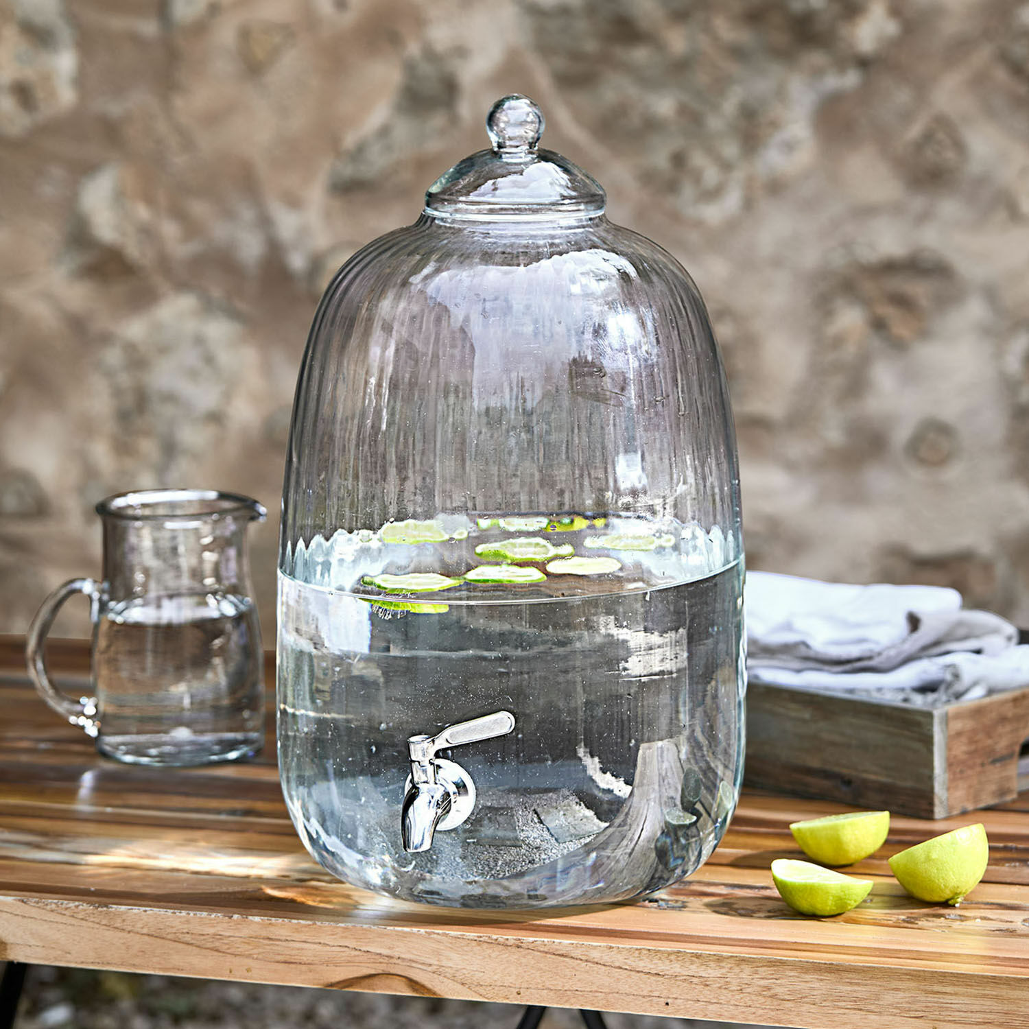 Dispensador de bebidas Alindor Dispensador de agua de vidrio transparente con grifo y tapa, rodajas de lima flotando sobre mesa