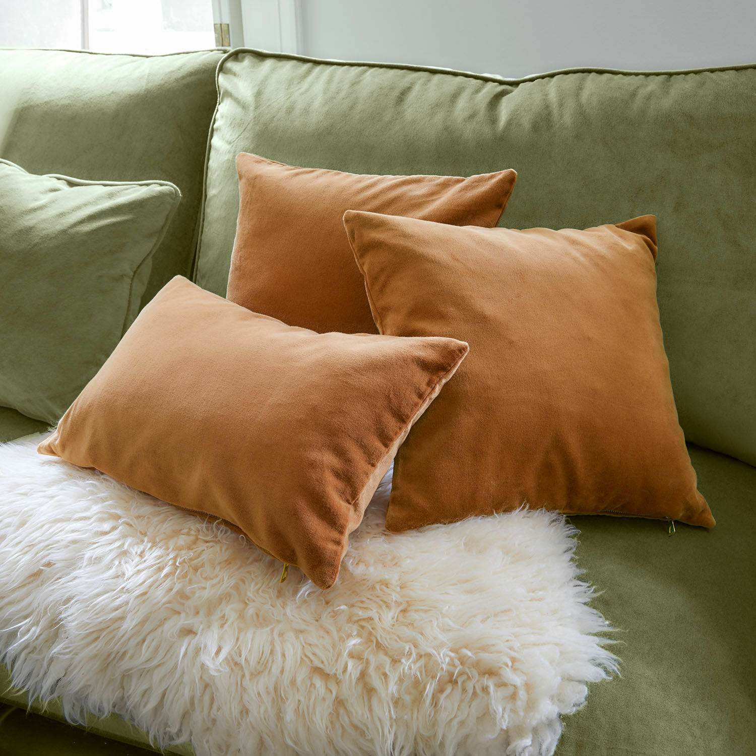 Set de 3 fundas de cojín Shahrine Conjunto de tres cojines marrones de tela suave sobre sofá verde con manta blanca de piel sintética