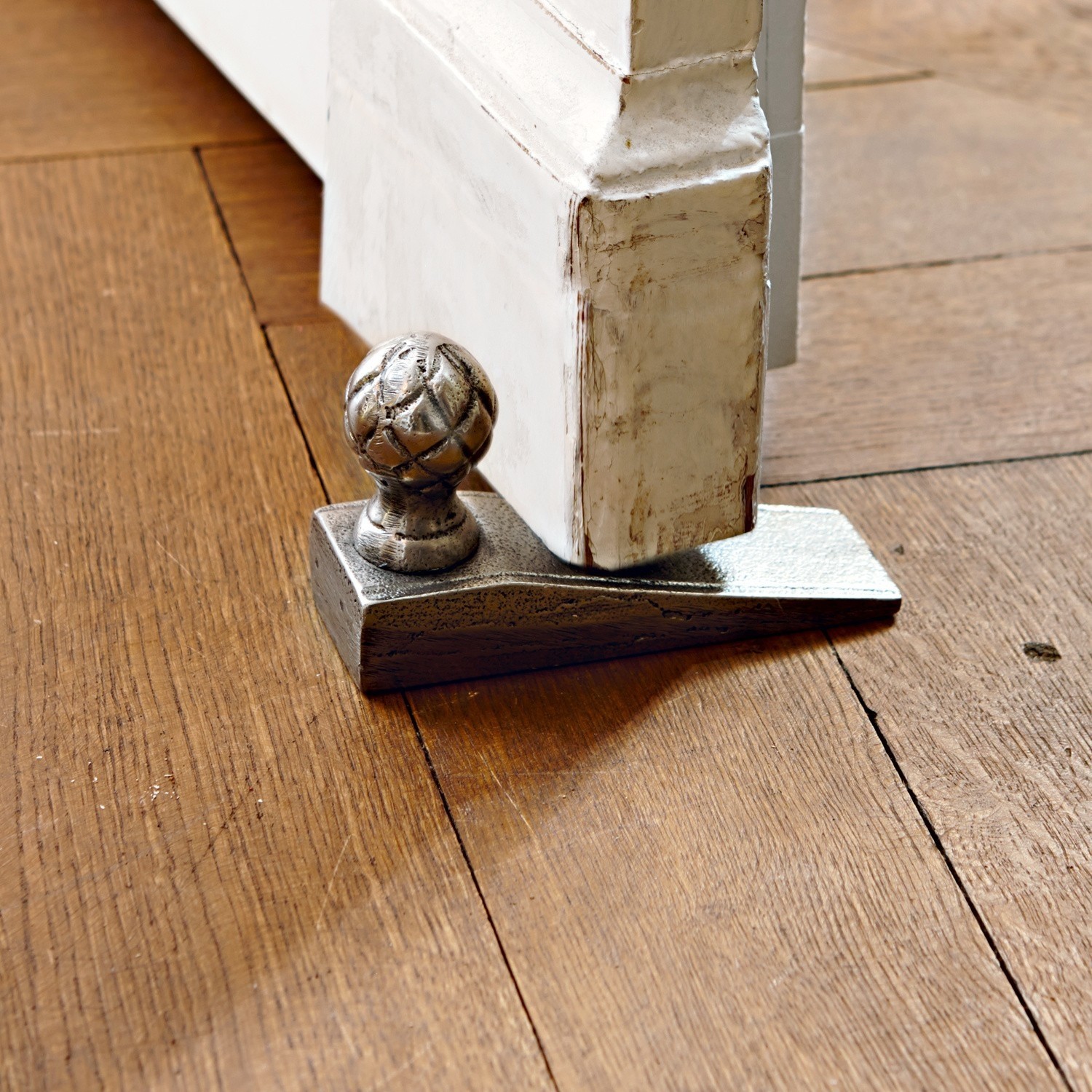 Tope de puerta Broche Cuña de puerta metálica plateada sobre suelo de madera protege puerta blanca