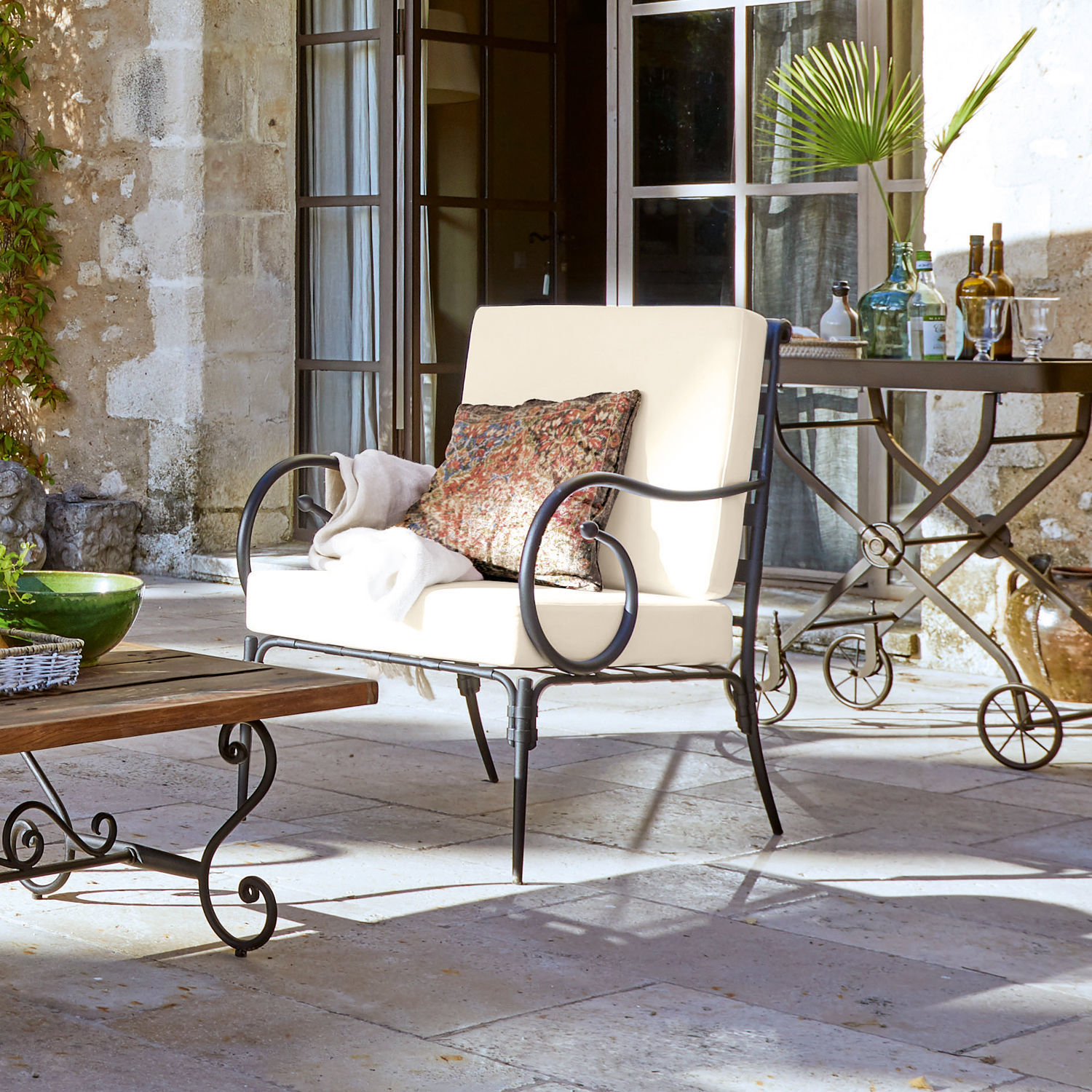 Sofá de jardín de metal con cojines crema y cojín decorativo en patio de piedra