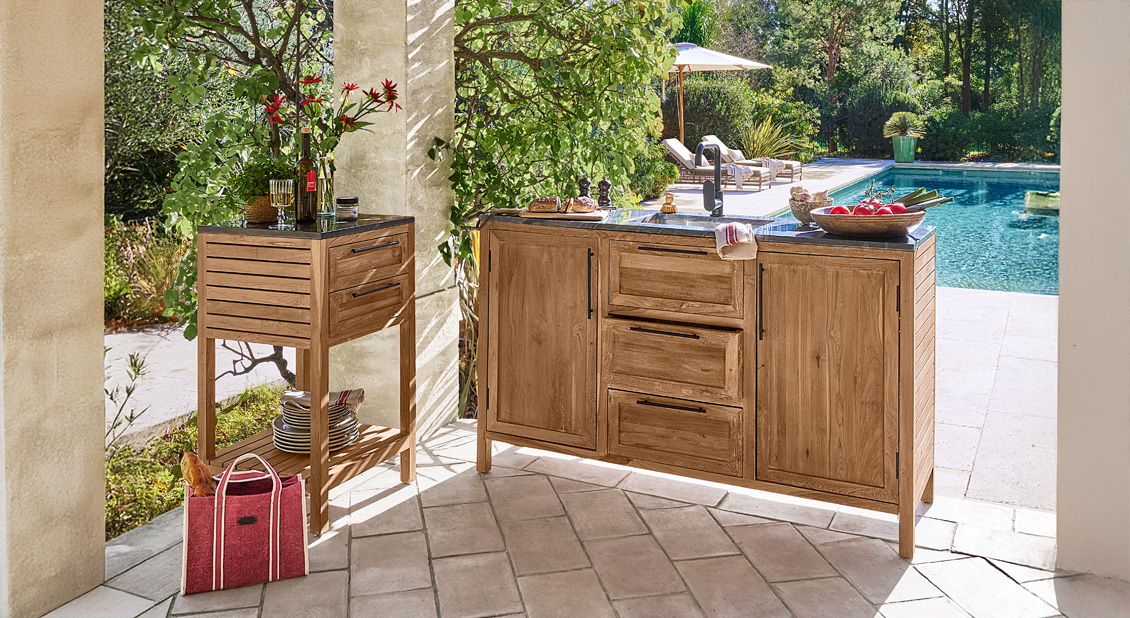 Cocina exterior de madera de teca con encimera negra y armarios en terraza junto a piscina