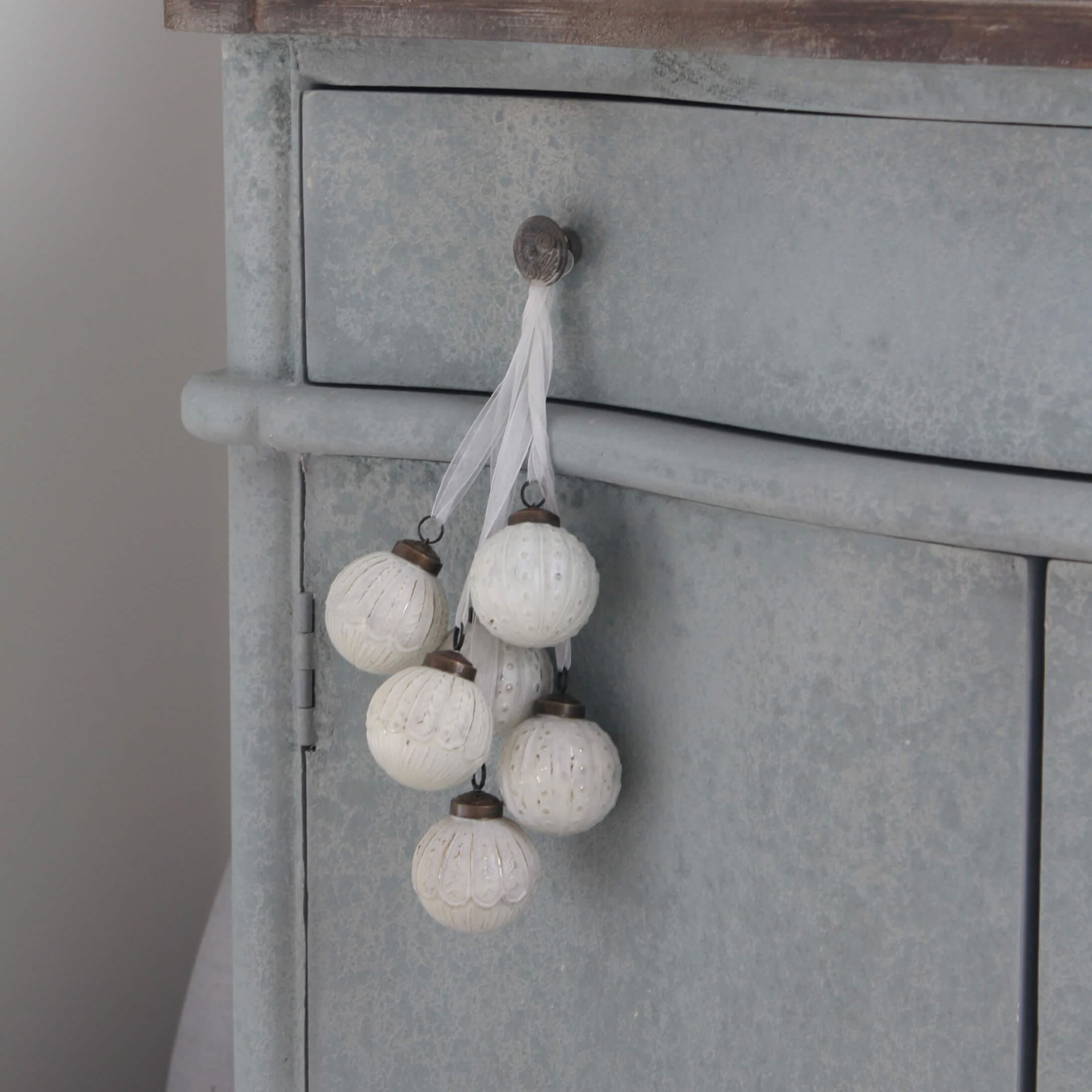 Conjunto de bolas decorativas blancas con diseño delicado colgadas en mueble metálico gris