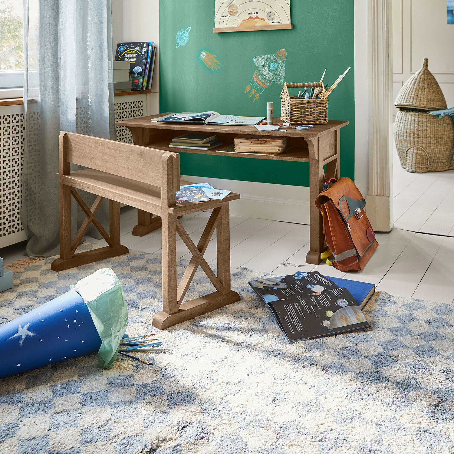 Escritorio y banco de madera en habitación infantil con pizarra verde y libros sobre el espacio