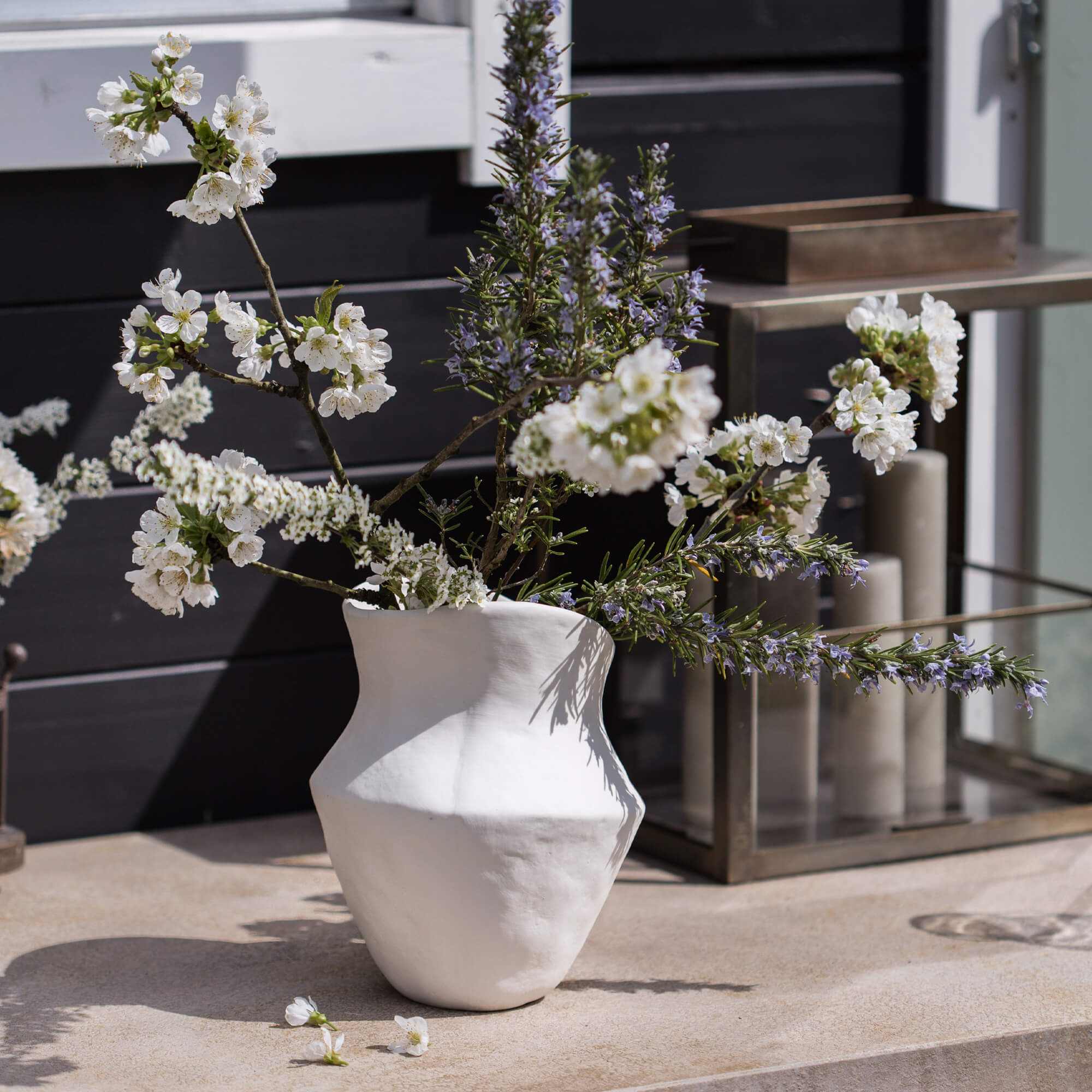 Jarrón de cerámica blanca con flores y ramas sobre mesa decorativa exterior