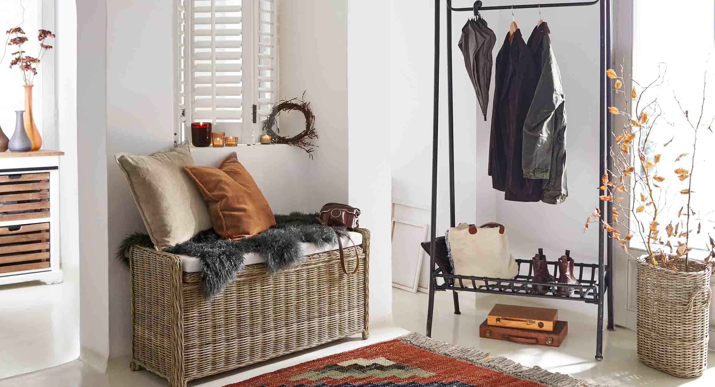 Recibidor con banco de mimbre, perchero metálico negro y decoración en tonos naturales y claros