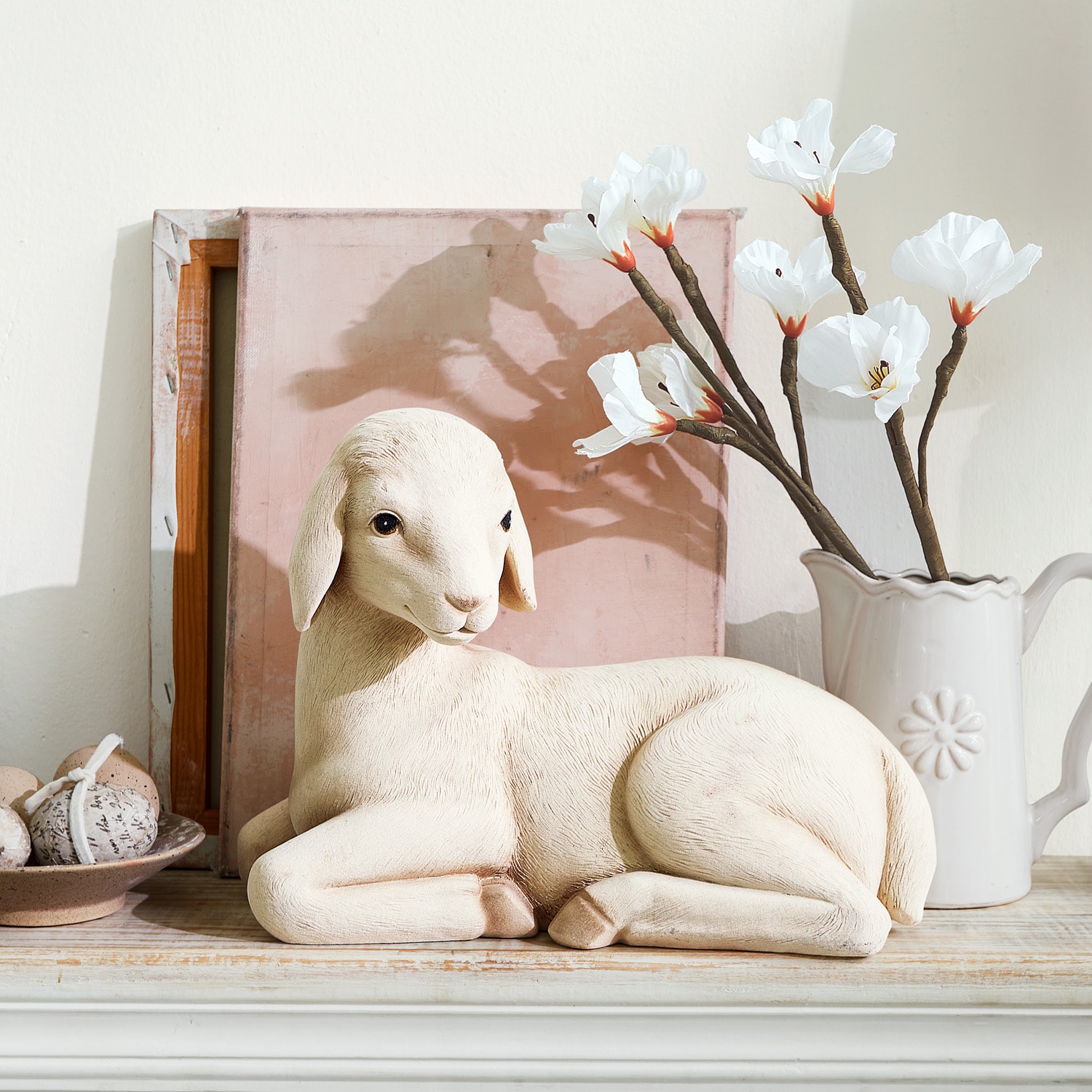 Figura decorativa de oveja en color claro sobre estante de madera con flores blancas