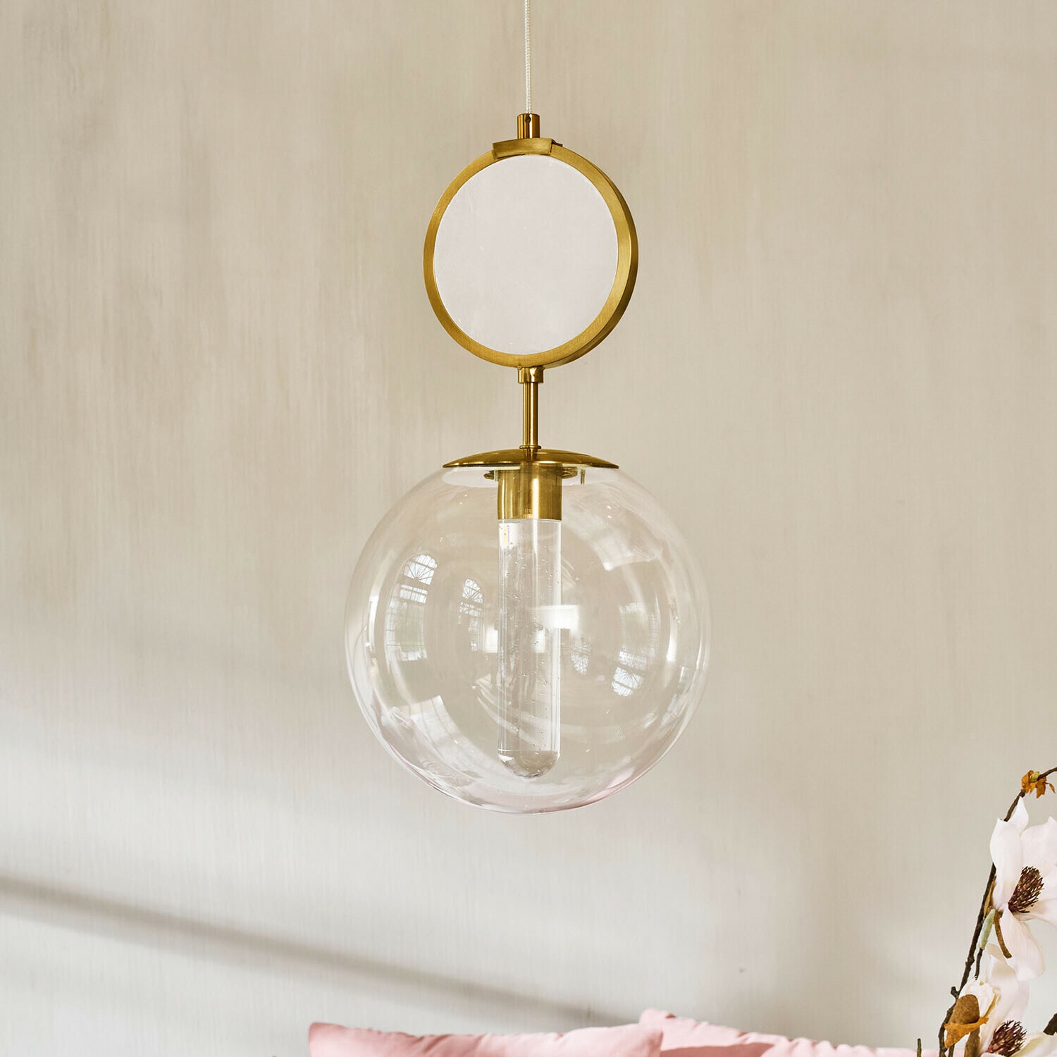 Lámpara LED colgante Corvane Lámpara colgante dorada con esfera de vidrio transparente y elemento decorativo circular sobre pared clara