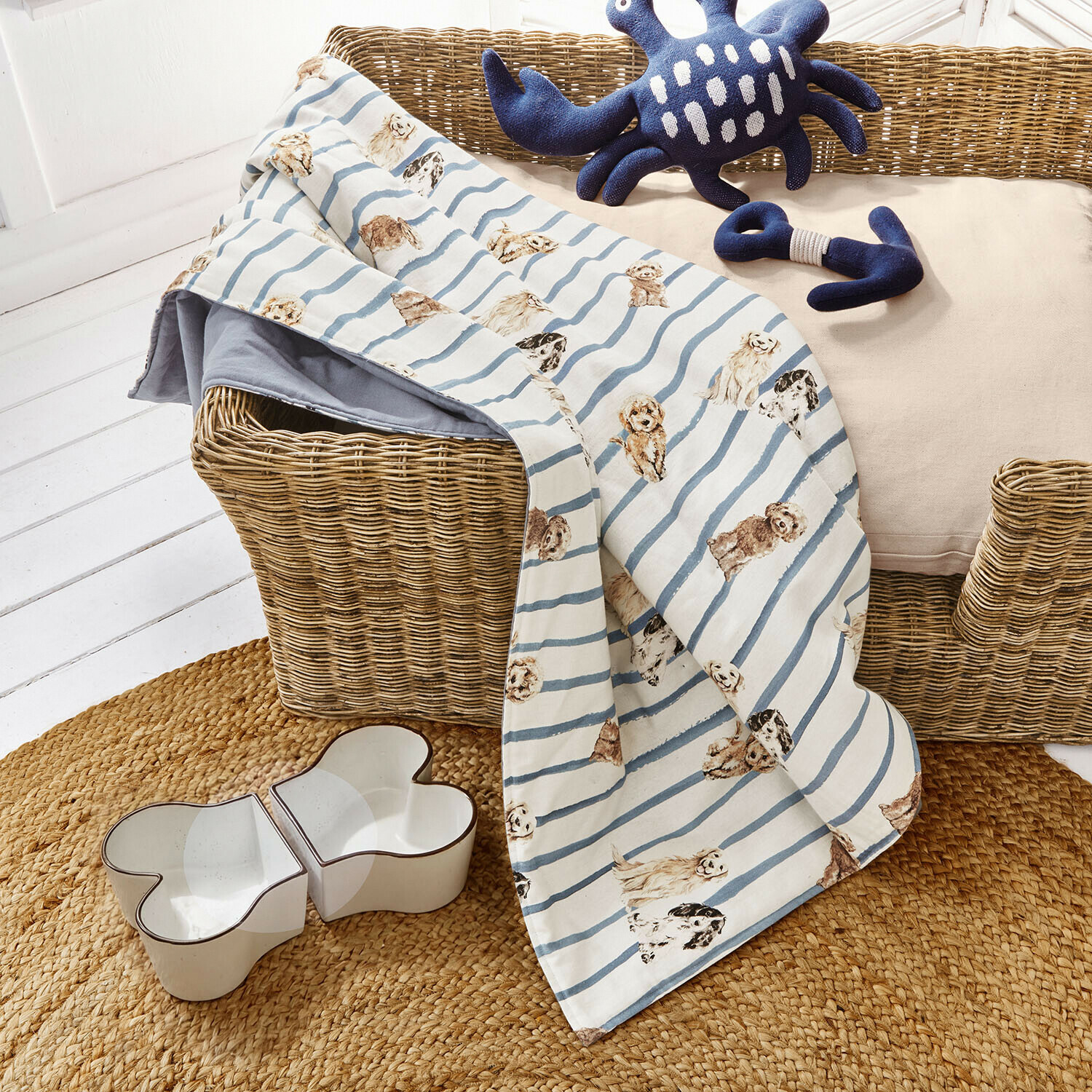 Manta para perros Schnuffelex Manta para perro con rayas azules y blancas y estampado de perros sobre cesto de mimbre con juguetes y comedero