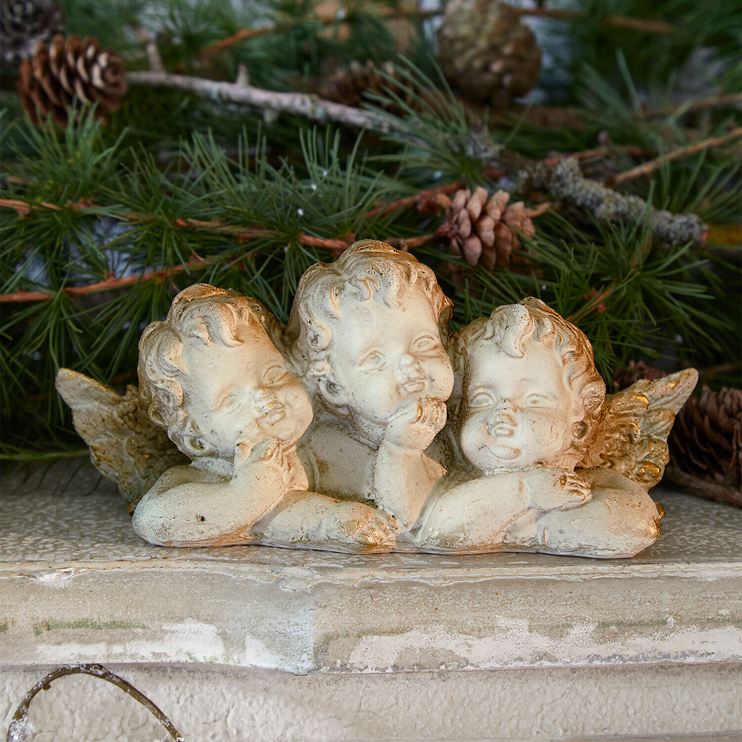 Ángeles decorativos Nivardo Figura de tres ángeles de piedra clara sobre fondo de ramas verdes de pino, decoración navideña