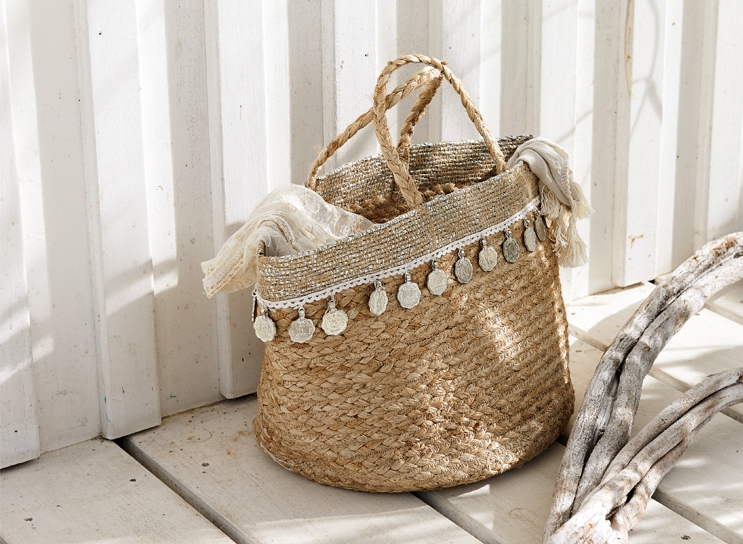Cesta bohemia de material natural trenzado con monedas decorativas y bufanda clara, decoración interior.