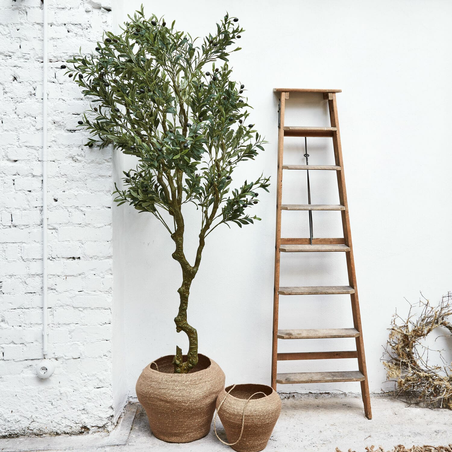 Planta decorativa Dambly Dos macetas de yute marrón natural junto a una escalera de madera frente a pared blanca