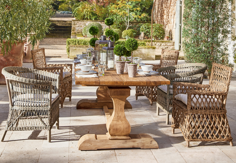 Mesa de jardín de madera con sillas de mimbre y decoración vegetal en terraza de estilo mediterráneo