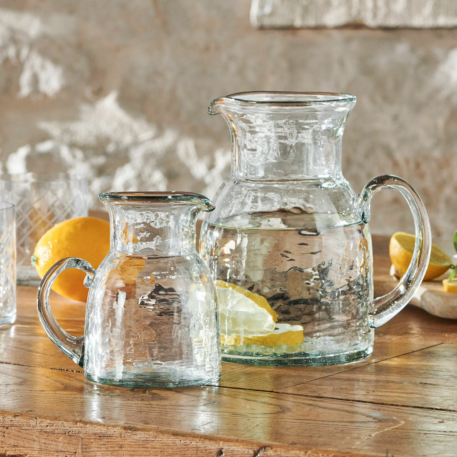Set de 2 jarras Zamirah Jarras de vidrio transparente con agua y rodajas de limón sobre mesa de madera rústica