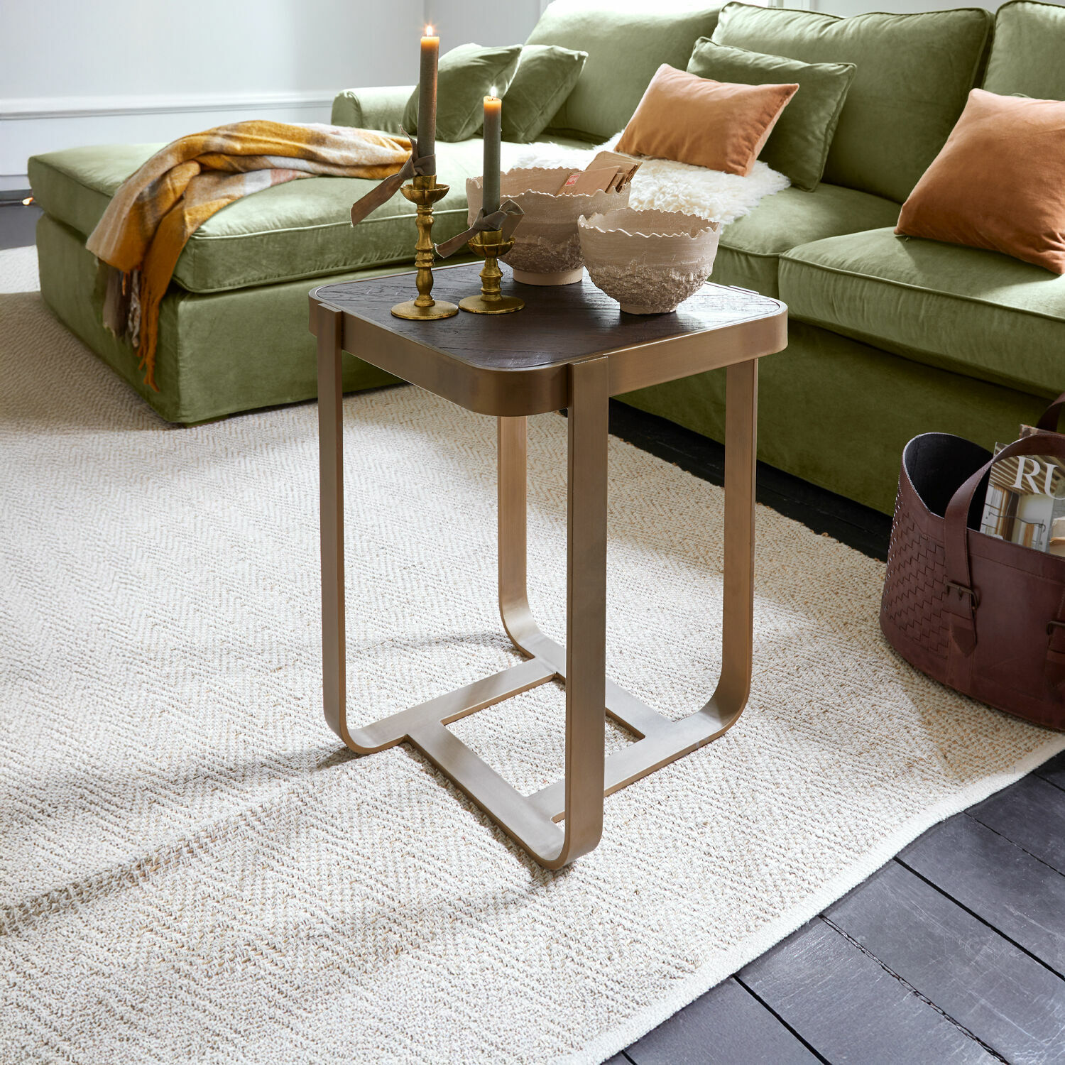 Mesa auxiliar Cranthorpe Mesa auxiliar con estructura metálica y tablero de madera oscura sobre alfombra clara en salón con sofá verde