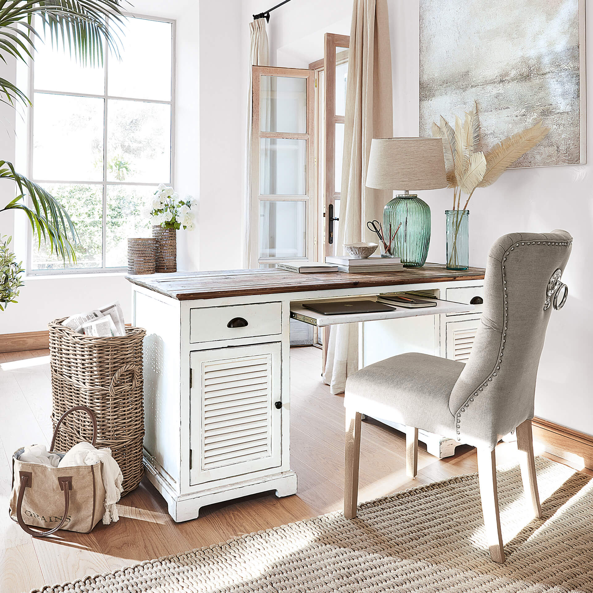Escritorio de madera blanca con cajones y silla tapizada gris en habitación luminosa y acogedora