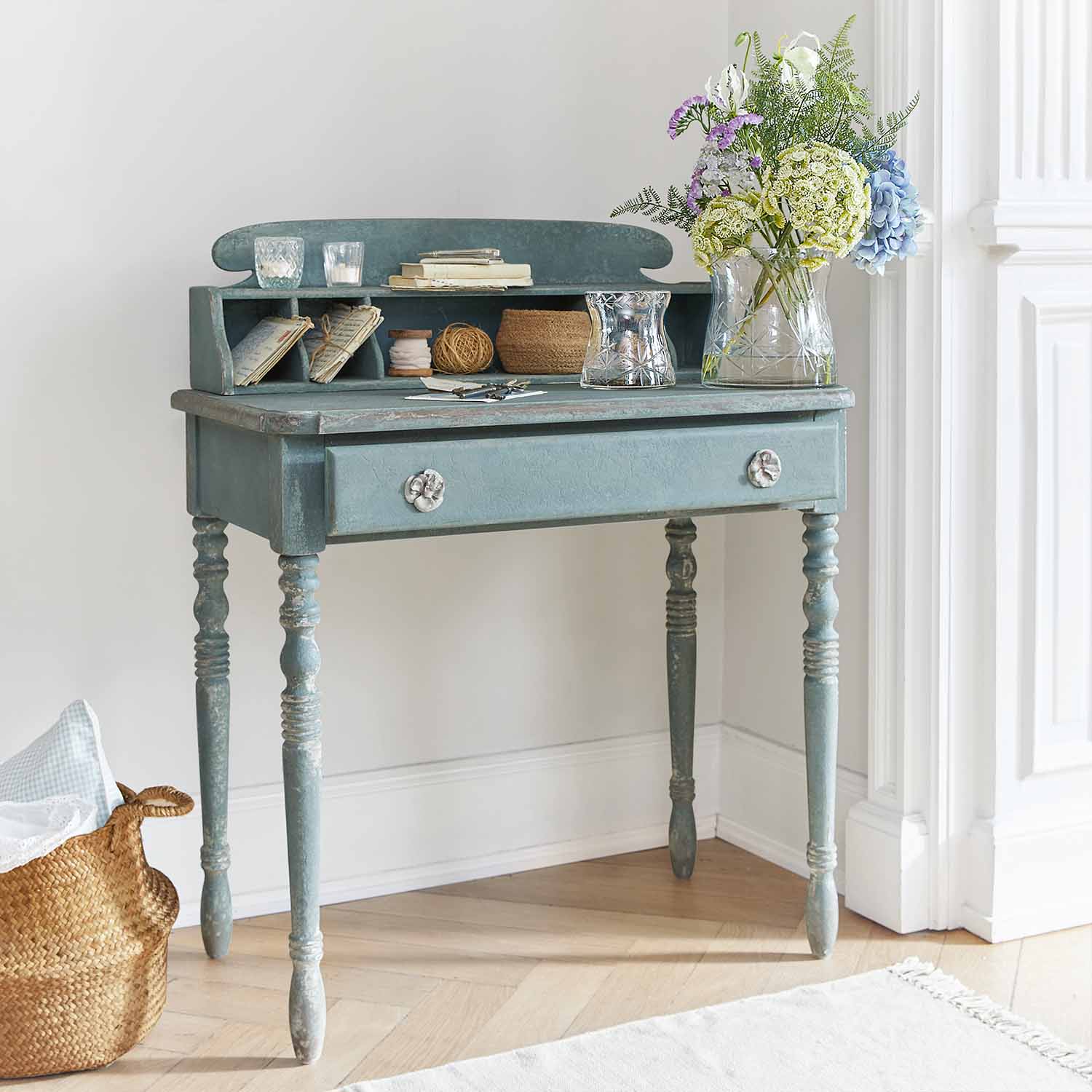 Escritorio de madera azul con cajón y estantes, decorado con jarrón de flores y velas