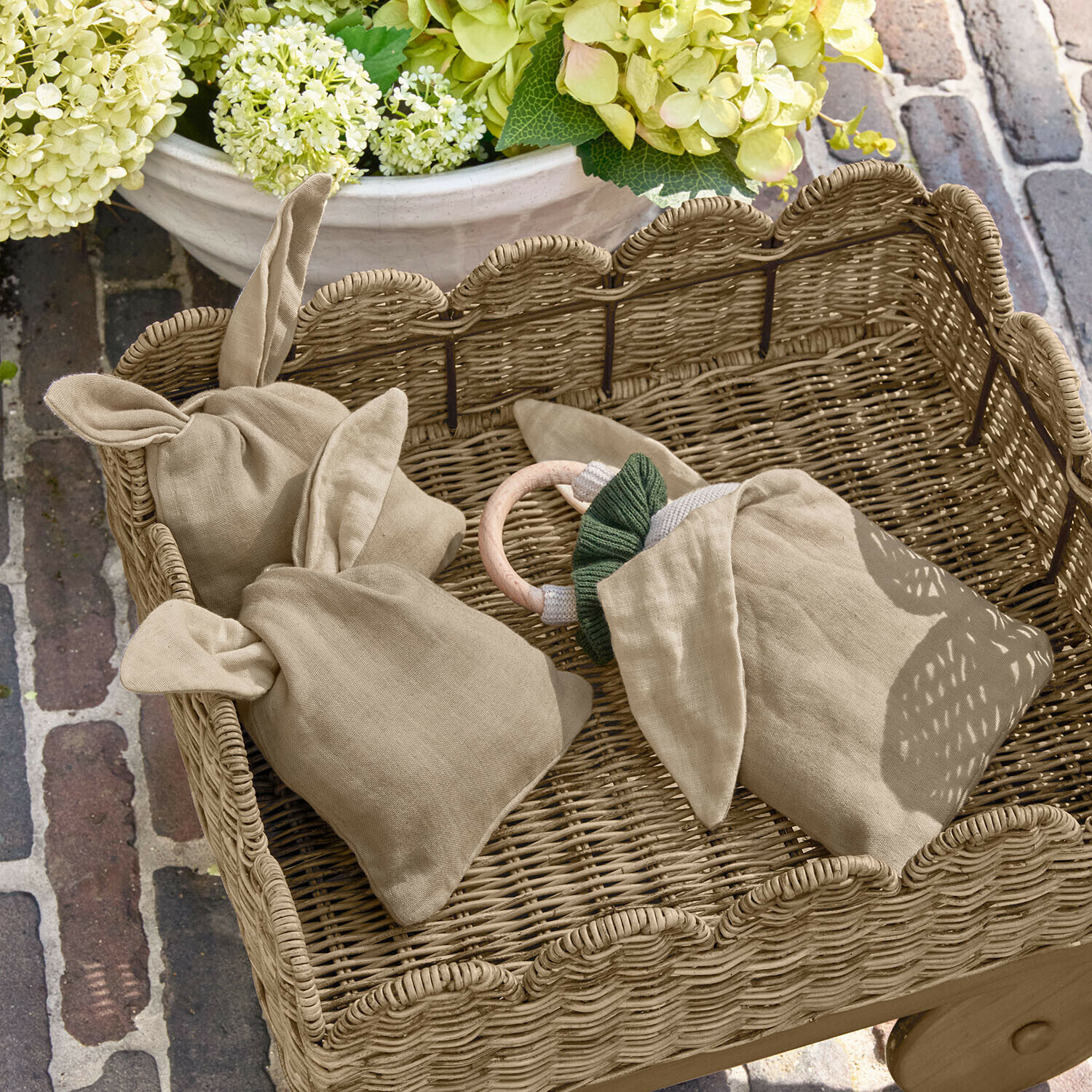 Set de 3 bolsitas Snugglewood Bolsa de lino beige con orejas en cesta de mimbre sobre fondo de flores y suelo de ladrillo