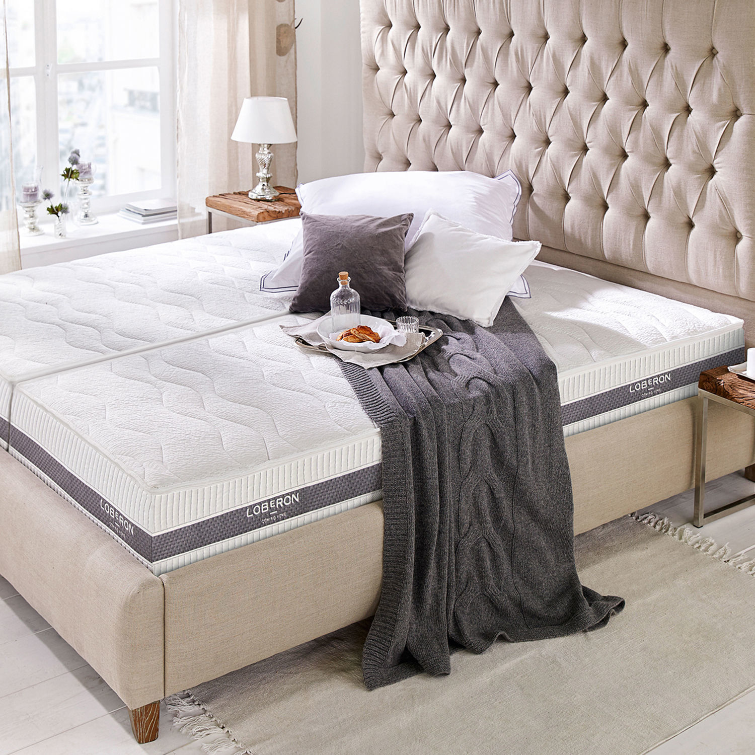 Colchón 90x200 Sevilha Cama tapizada beige con colchón blanco Loberon, manta gris y cojines en dormitorio luminoso
