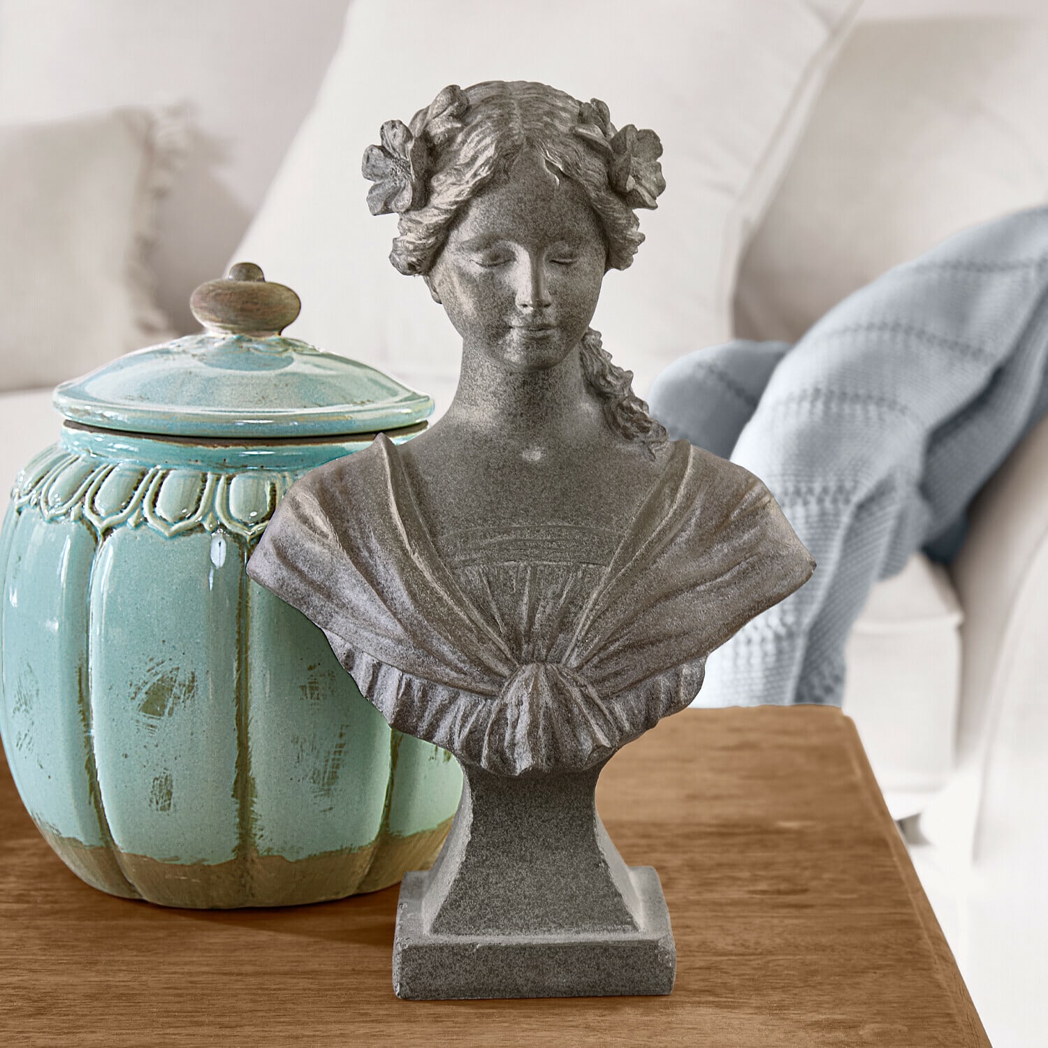 Busto Alexandra Busto femenino de piedra gris con flores en el cabello sobre mesa de madera junto a recipiente cerámico turquesa