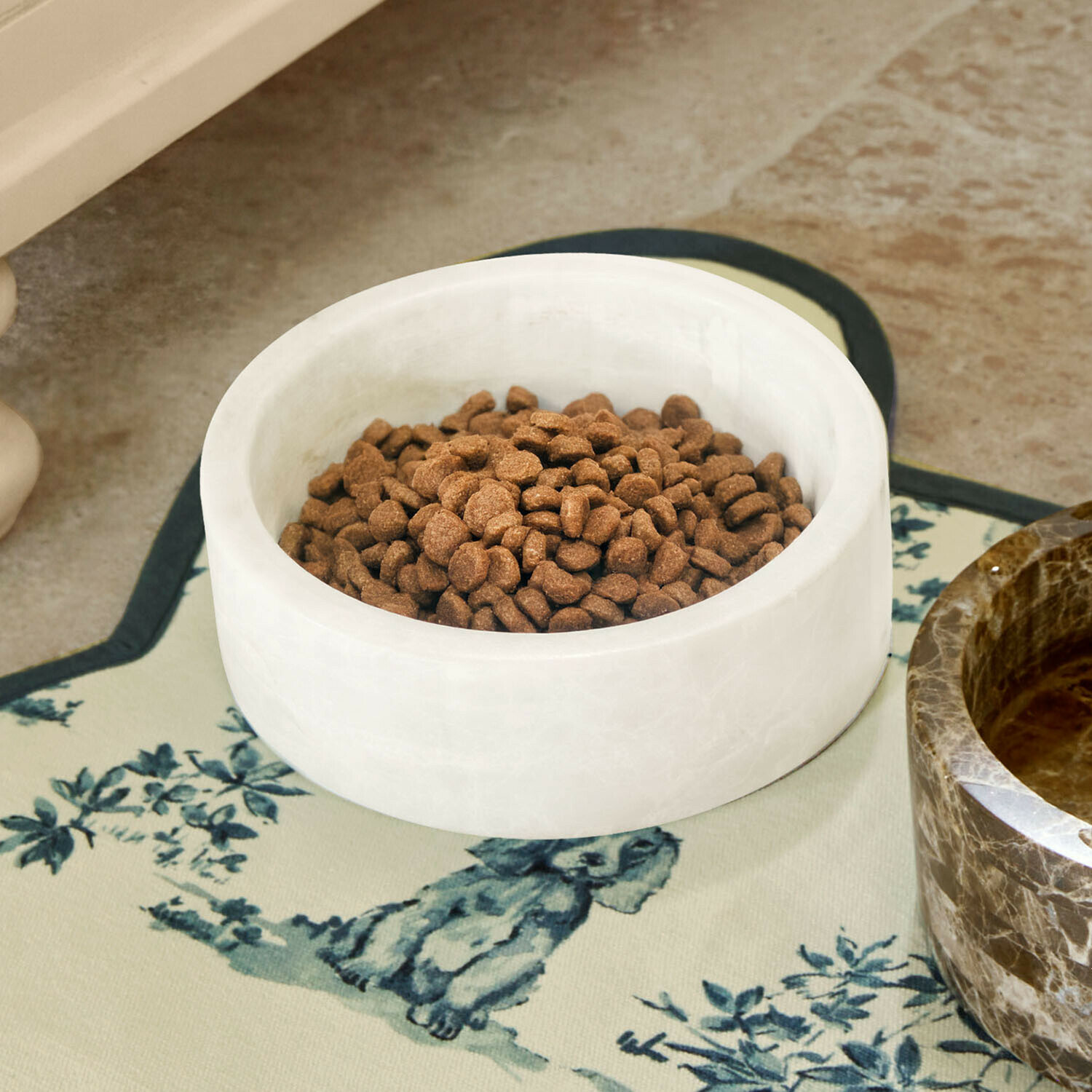 Cuenco de mármol blanco con comida marrón para mascotas sobre alfombrilla decorativa con dibujo de perro
