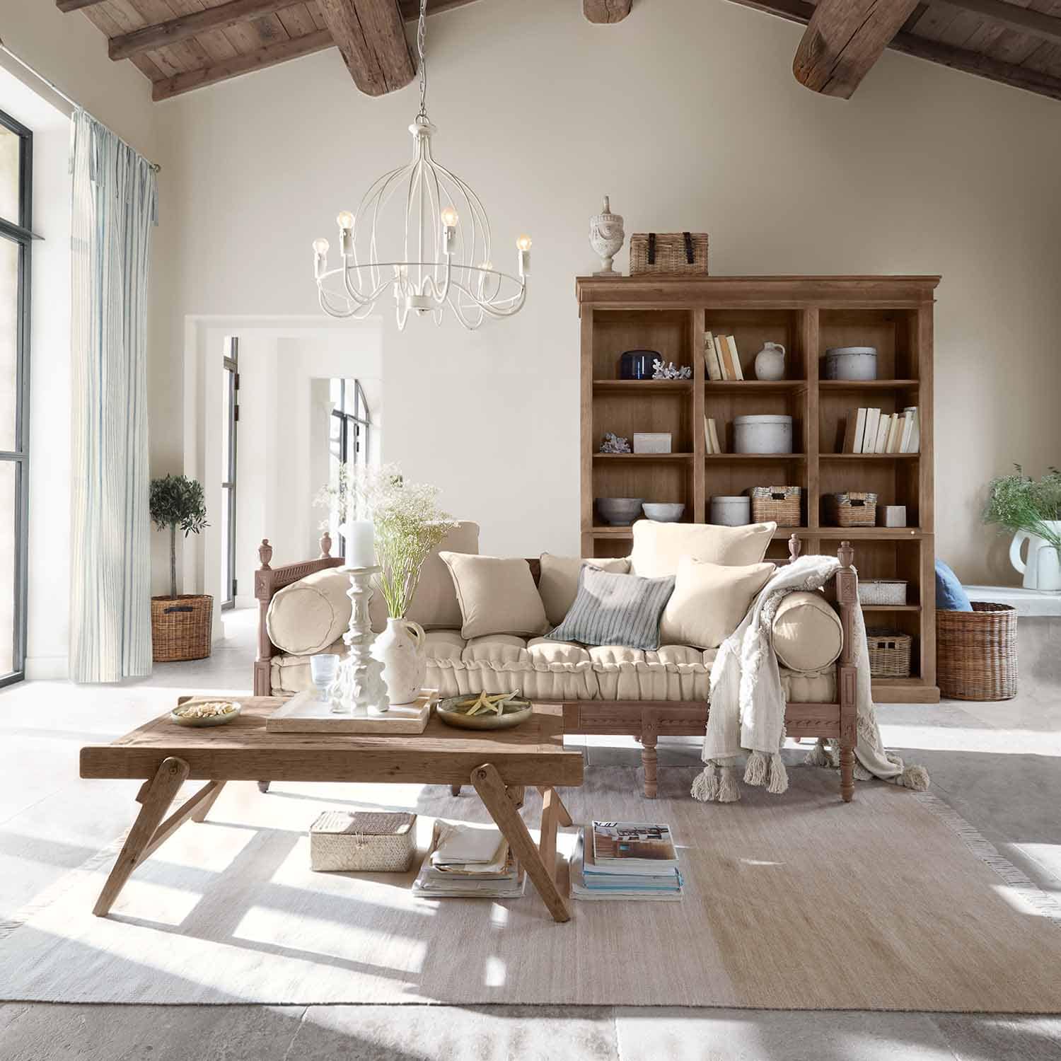 Sala acogedora con sofá de madera y cojines beige, mesa de centro rústica de madera y estantería al fondo