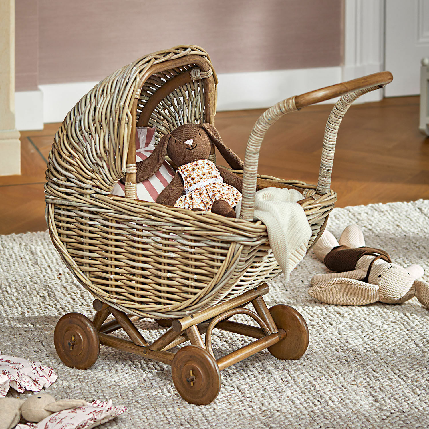 Cochecito de muñeca Fableton Cochecito de mimbre con ruedas de madera y peluches sobre alfombra en habitación infantil
