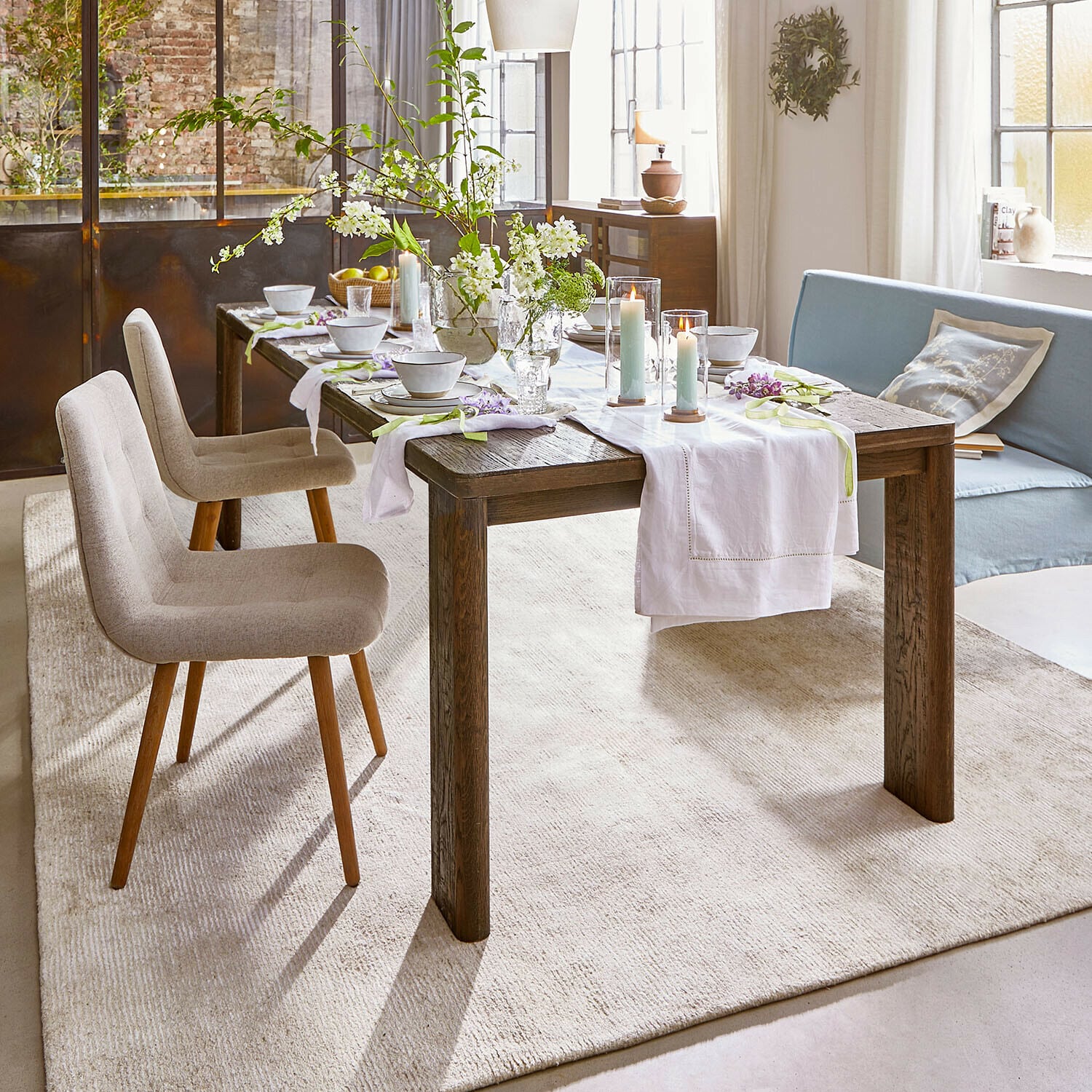 Mesa Gianoro Mesa de comedor rústica de madera oscura con camino de mesa blanco y velas en salón luminoso