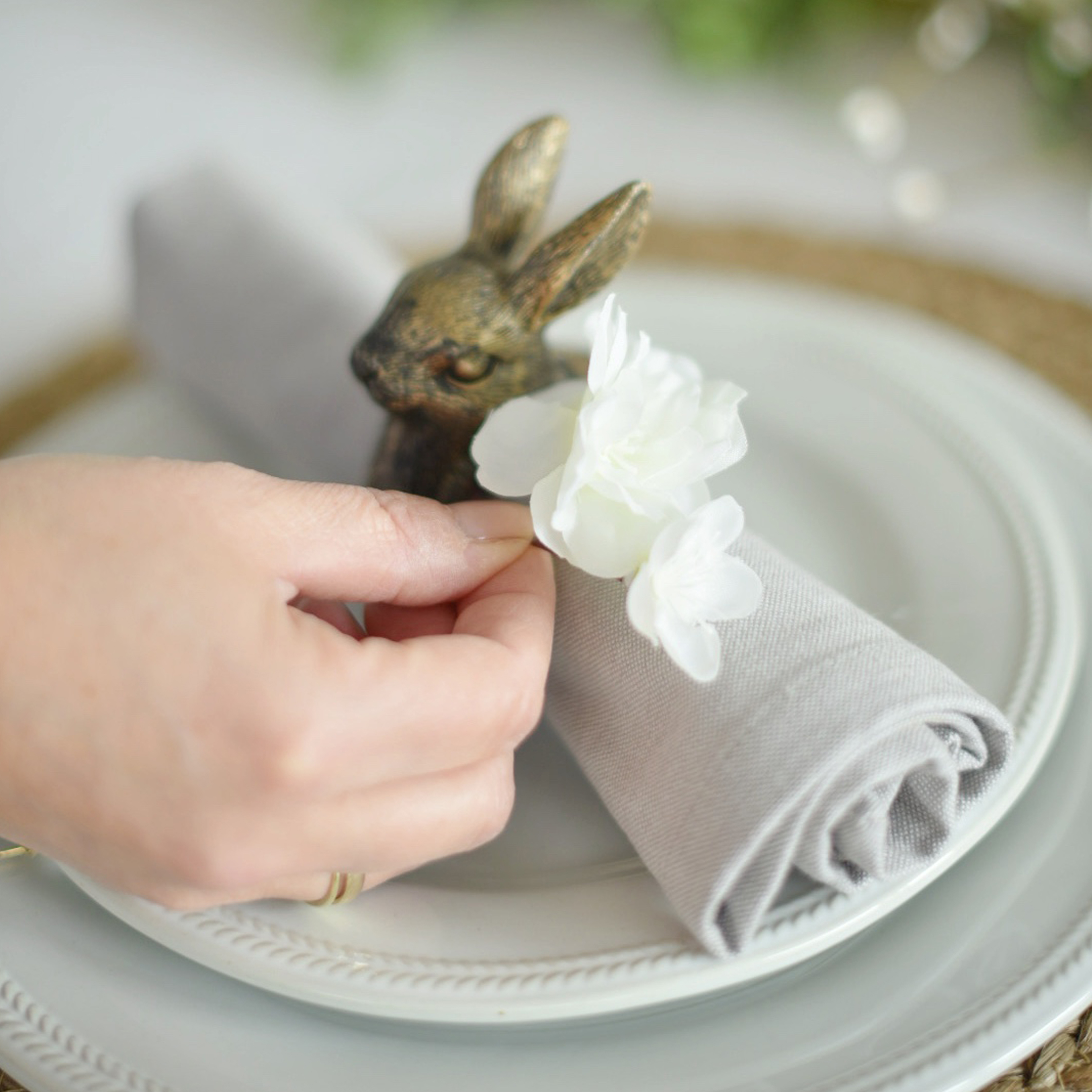 Anillo de servilleta de lino gris con flor blanca y decoración de conejo de latón en plato blanco