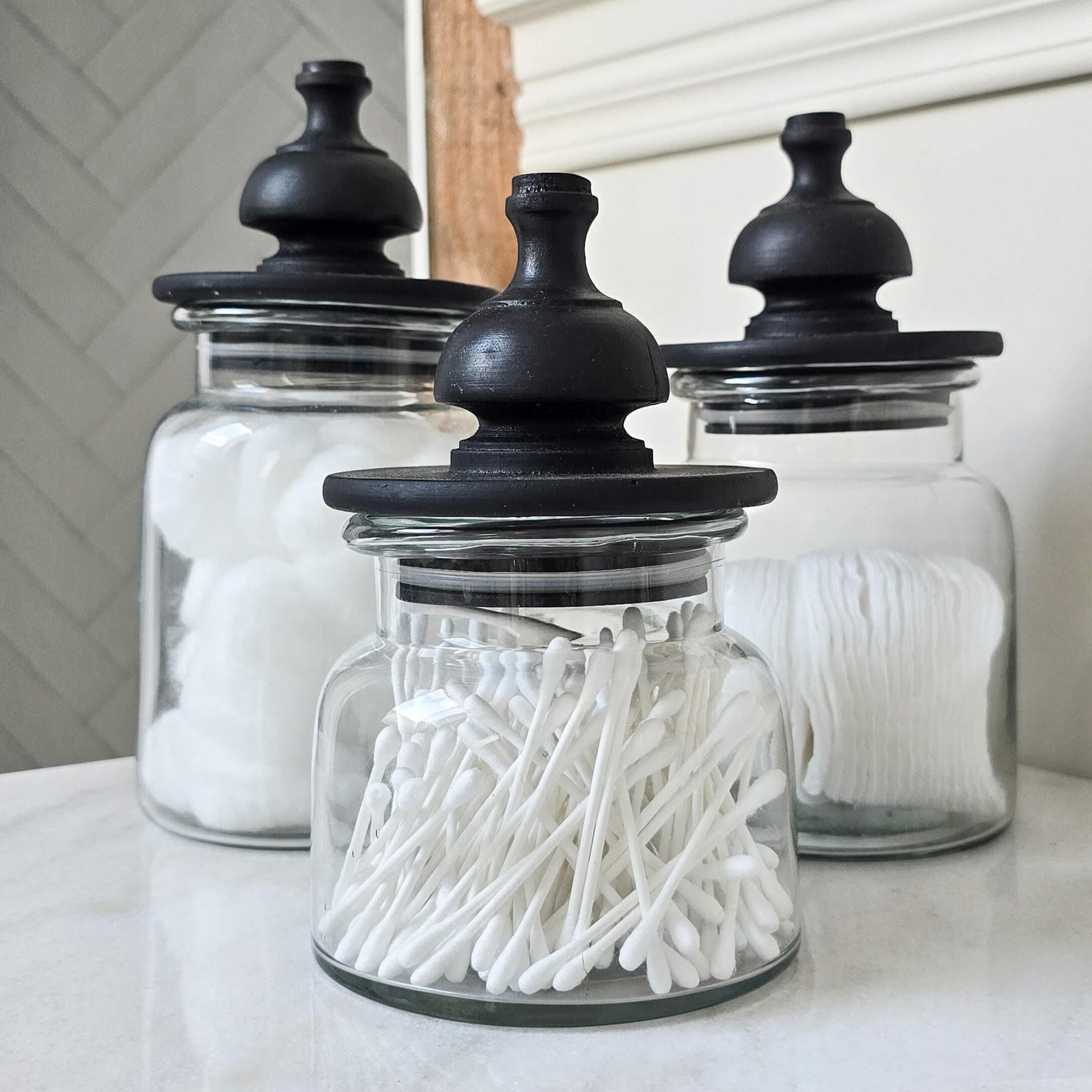Frascos de vidrio con tapas negras para algodones y bastoncillos en baño
