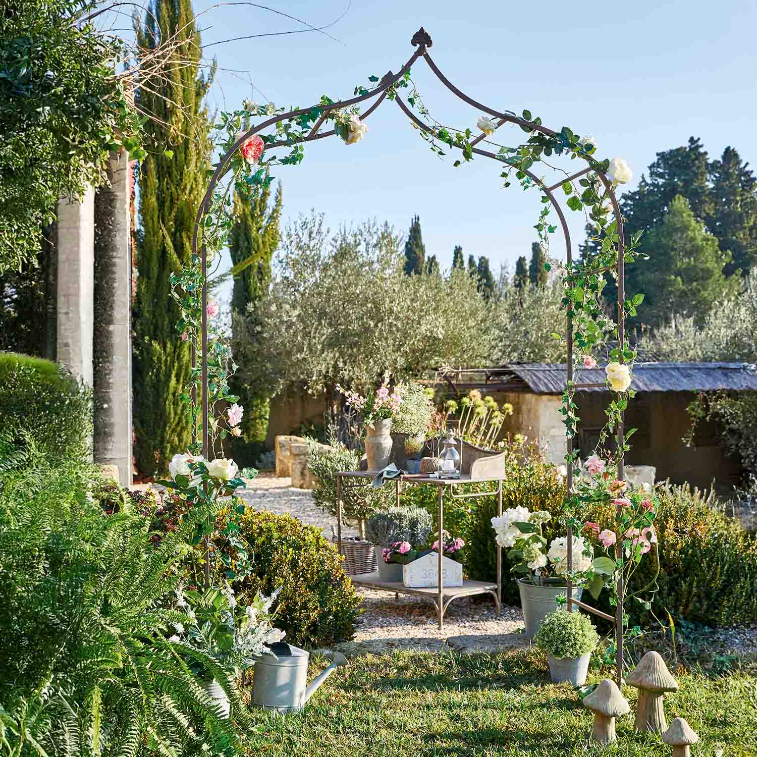 Pérgola de jardín de metal con hojas verdes y flores rosas en jardín soleado