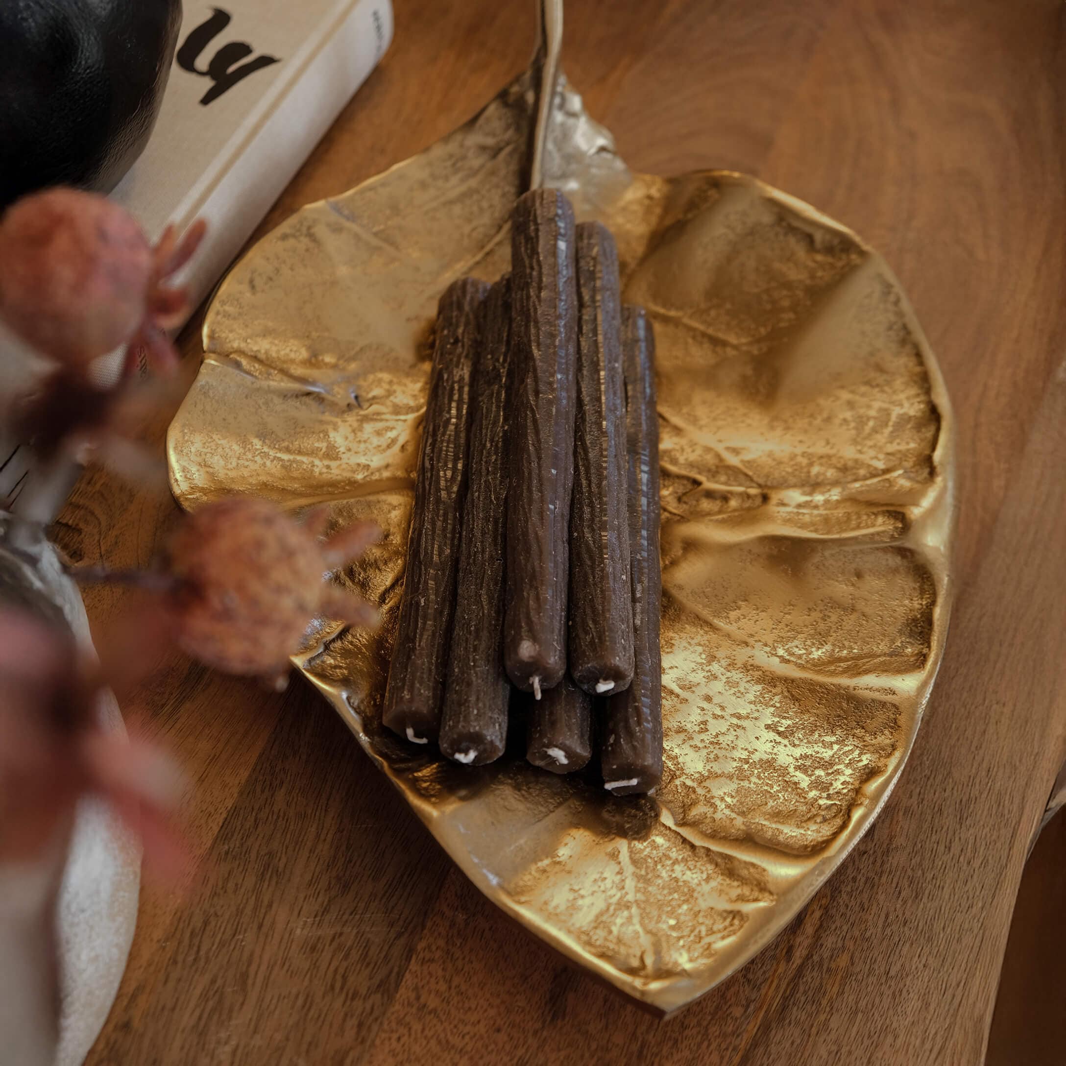 Bandeja metálica dorada en forma de hoja con velas decorativas marrones sobre mesa de madera