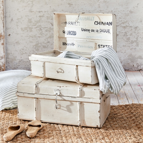 Cajas de madera blancas envejecidas con textiles a rayas y zapatillas sobre alfombra de yute
