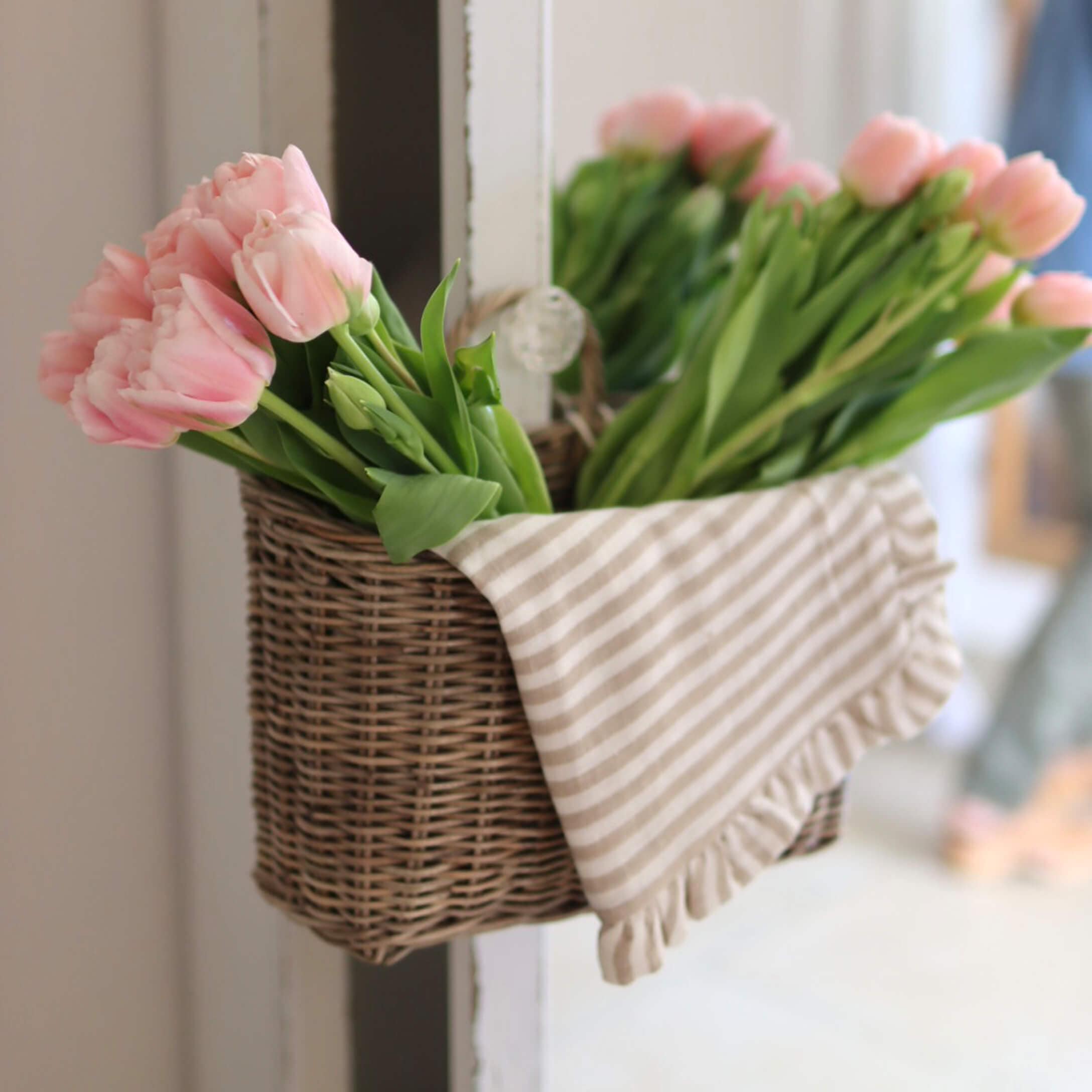 Cesta de mimbre con tulipanes rosas y paño de algodón a rayas para decoración interior