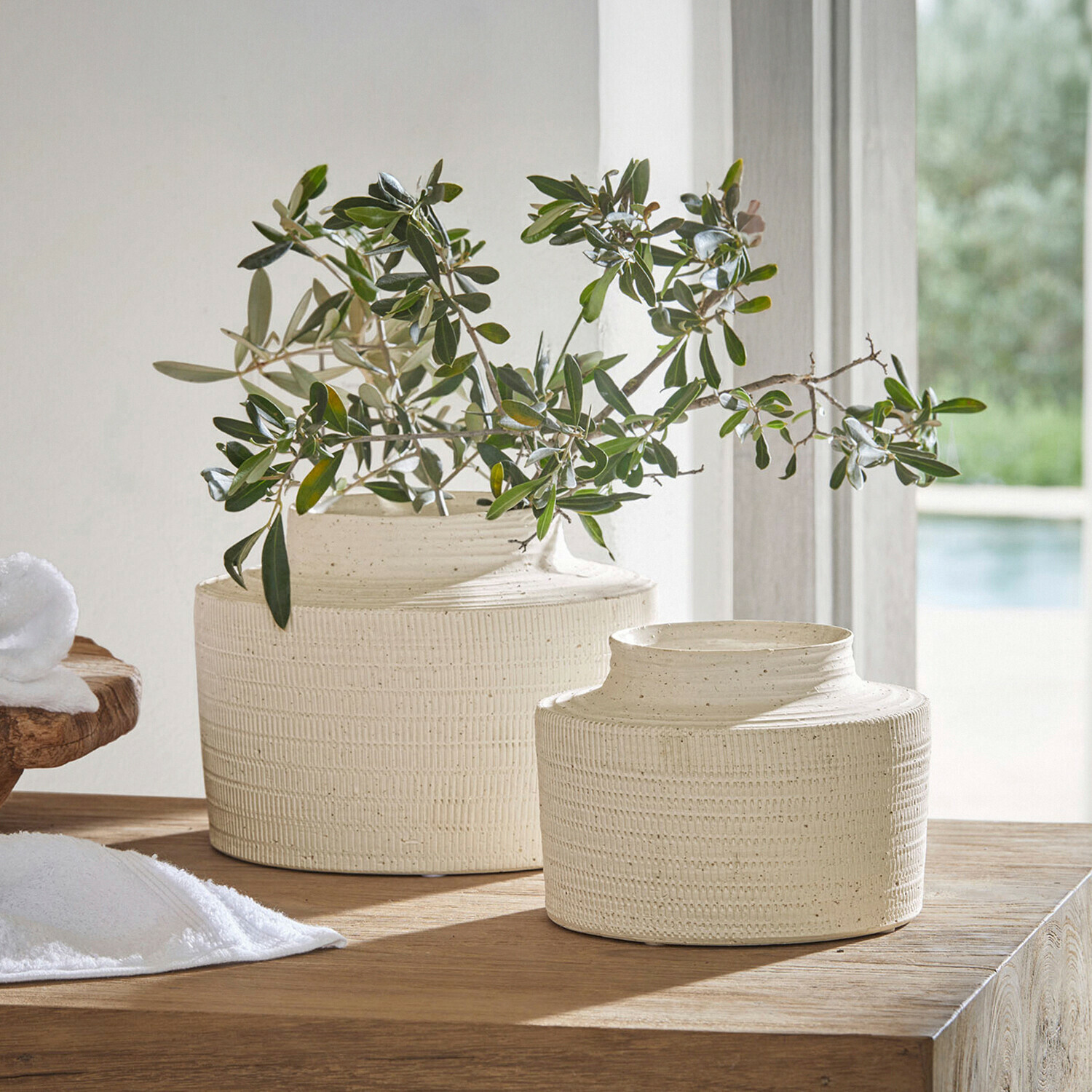Set de 2 jarrones Délavrie Dos jarrones de cerámica crema con textura sobre mesa de madera con ramas verdes