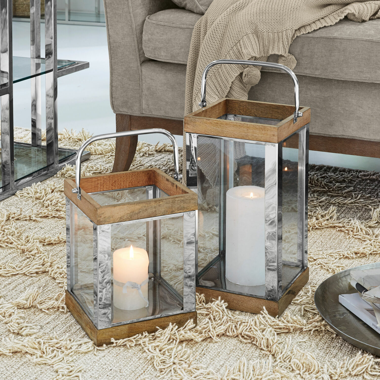 Set de 2 faroles Harpers Dos faroles de madera y metal con paredes de vidrio y velas blancas sobre alfombra beige