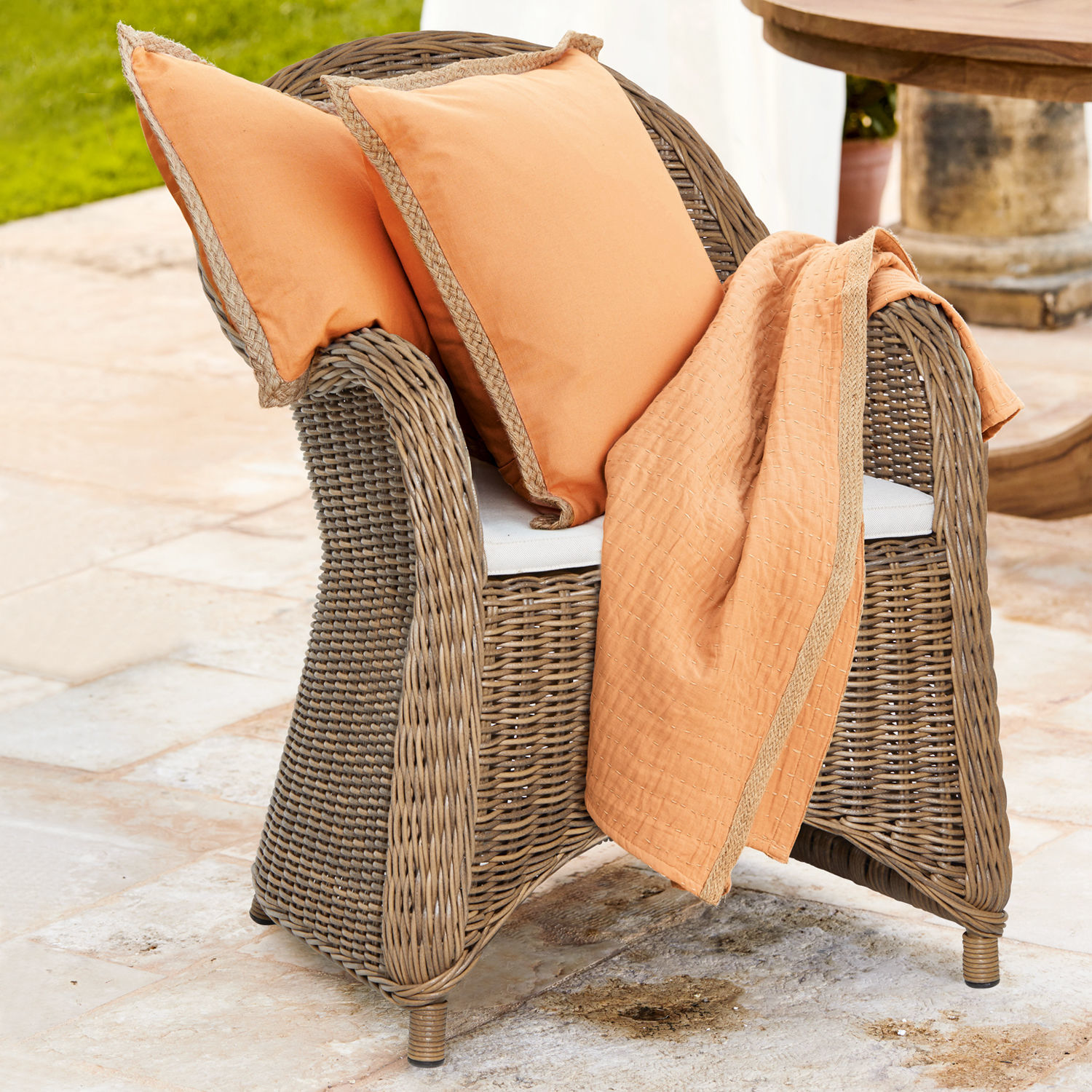 Sillón de ratán con cojines y manta naranja para terraza o jardín