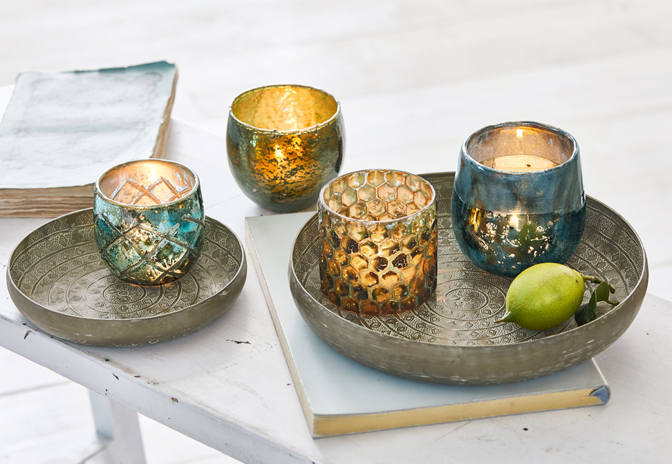 Bandejas metálicas orientales con portavelas decorativos dorados y turquesas sobre mesa blanca