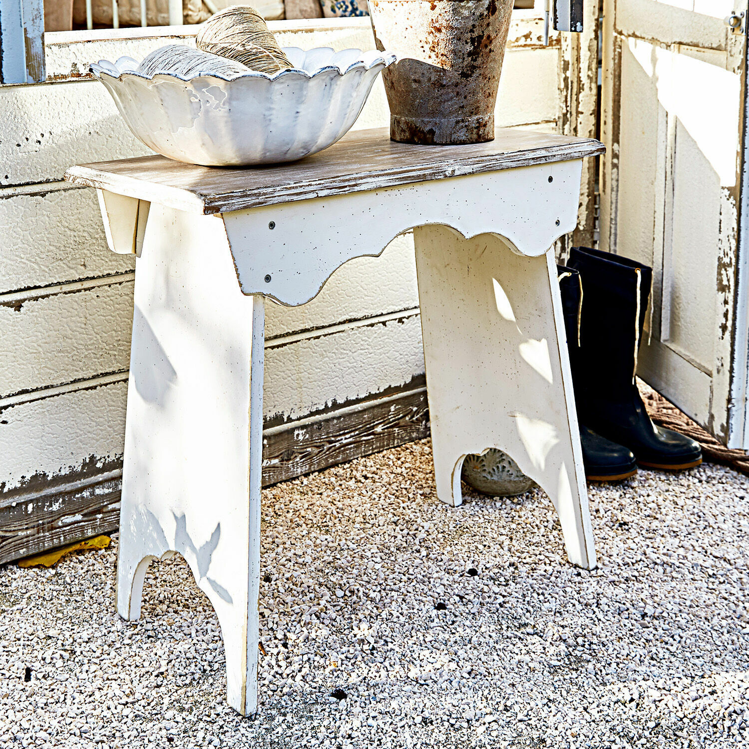 Taburete Fria Mesa de madera blanca envejecida sobre grava con cuenco decorativo y botas negras al lado