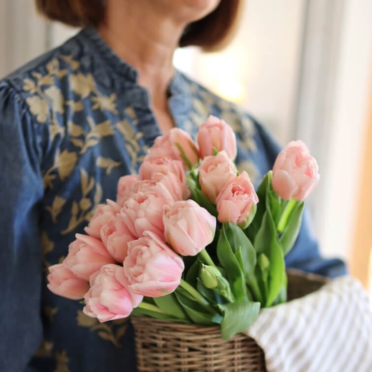 Ramo de tulipanes rosas en cesta de mimbre sostenida por mujer con blusa azul de flores