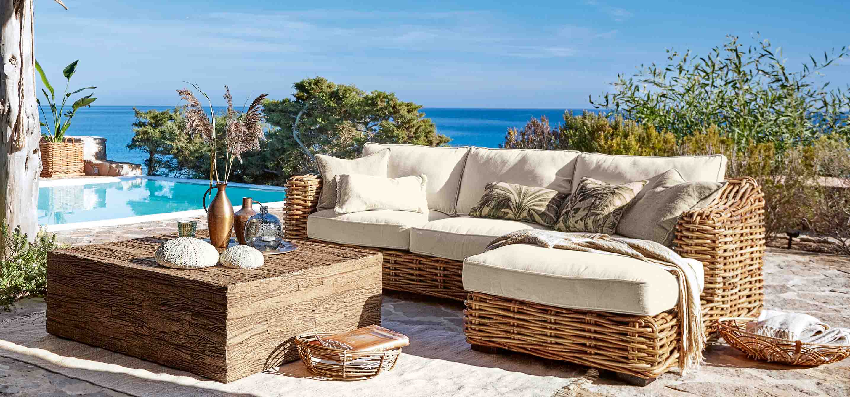 Conjunto de muebles de jardín de ratán con cojines crema junto a piscina con vista al mar