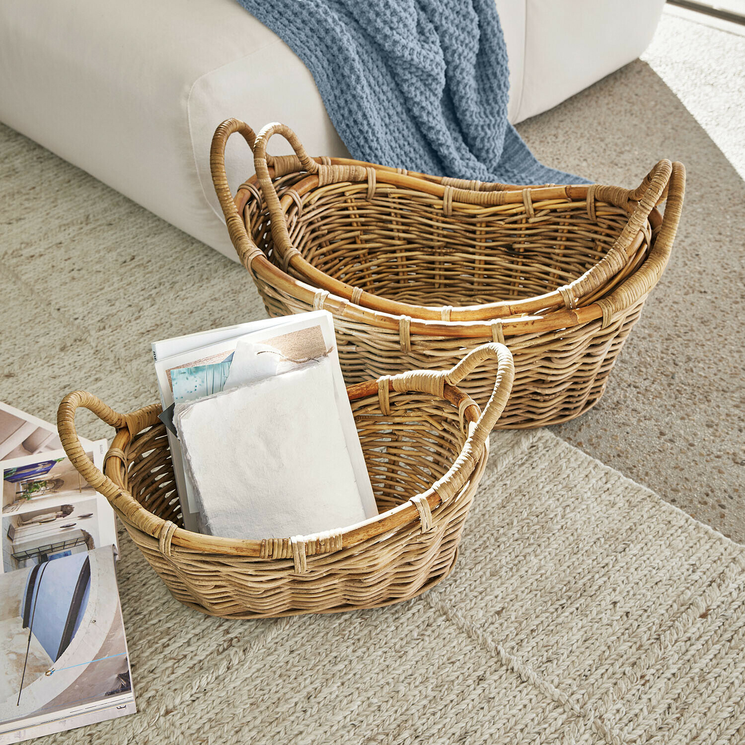 Dos cestas de mimbre natural sobre alfombra, una con revistas, almacenamiento práctico para el hogar