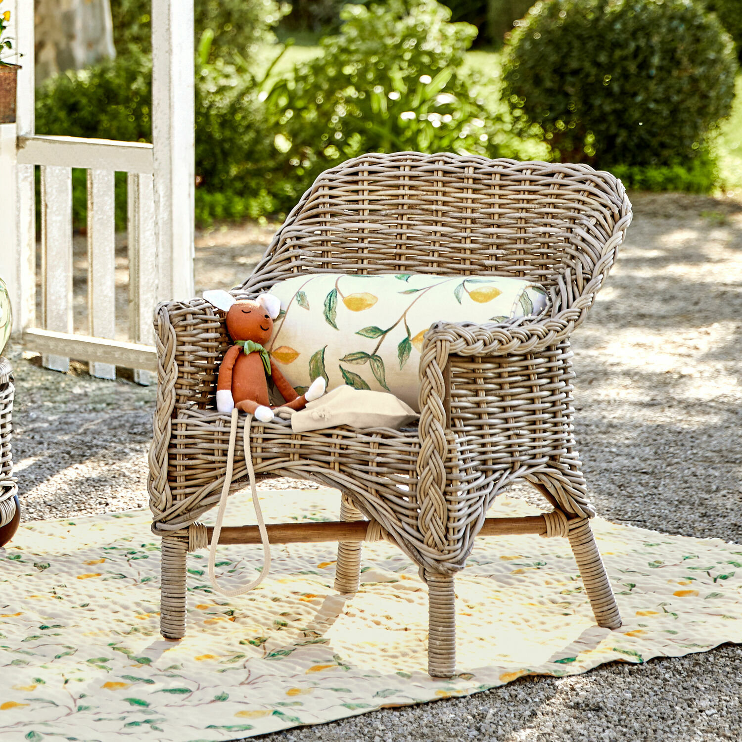 Silla infantil Narivena Sillón de ratán color natural con cojín de hojas y peluche en jardín soleado