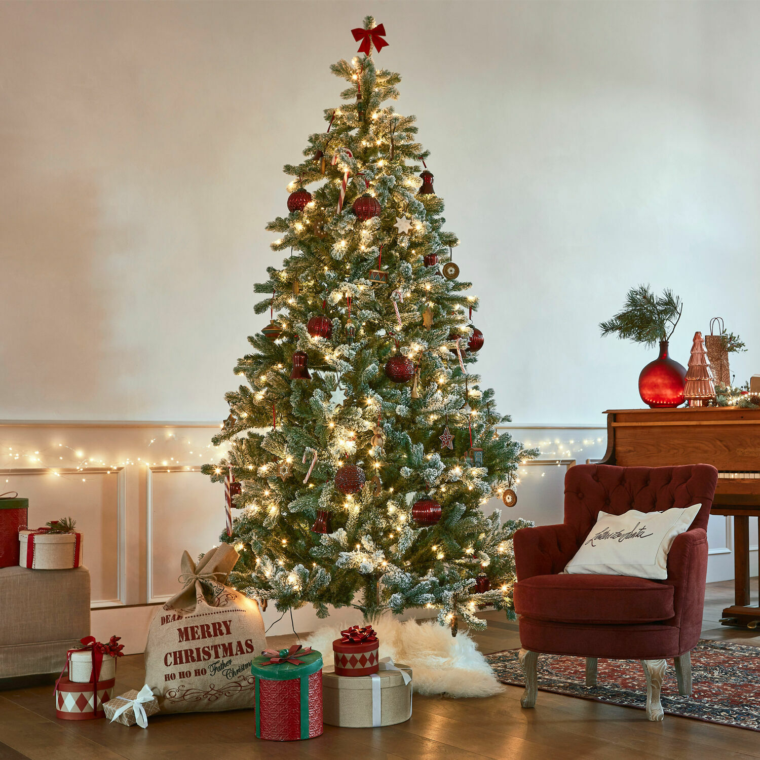 Árbol de Navidad Mannier Árbol de Navidad artificial nevado con adornos rojos y luces en una sala acogedora
