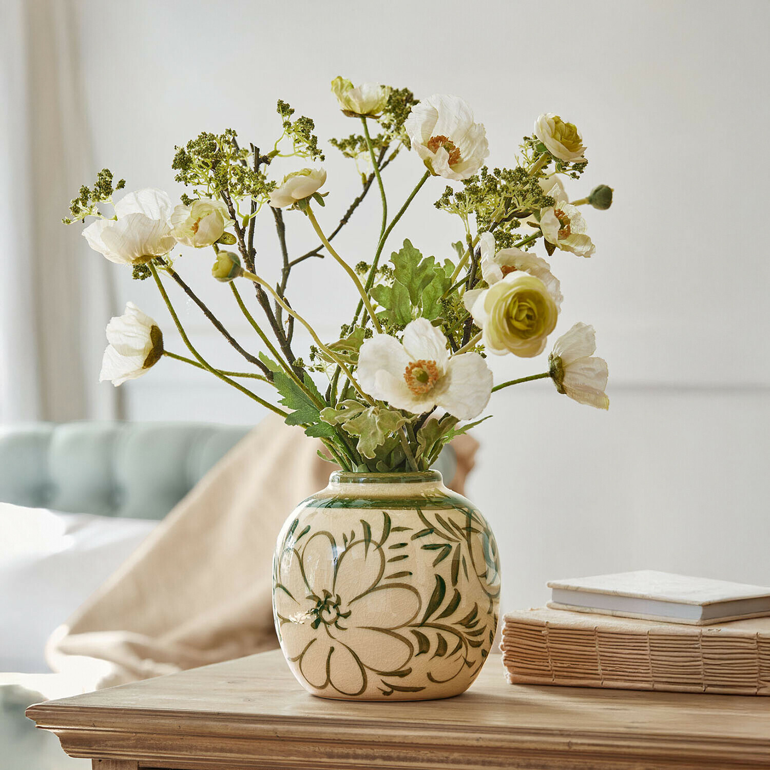 Jarrón Avignonel Jarrón de cerámica beige con motivos florales verdes y flores blancas artificiales sobre mesa de madera
