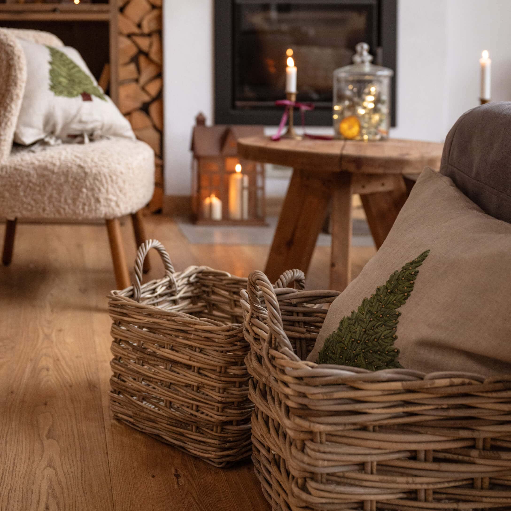Dos cestas de mimbre color natural sobre suelo de madera en salón acogedor con chimenea