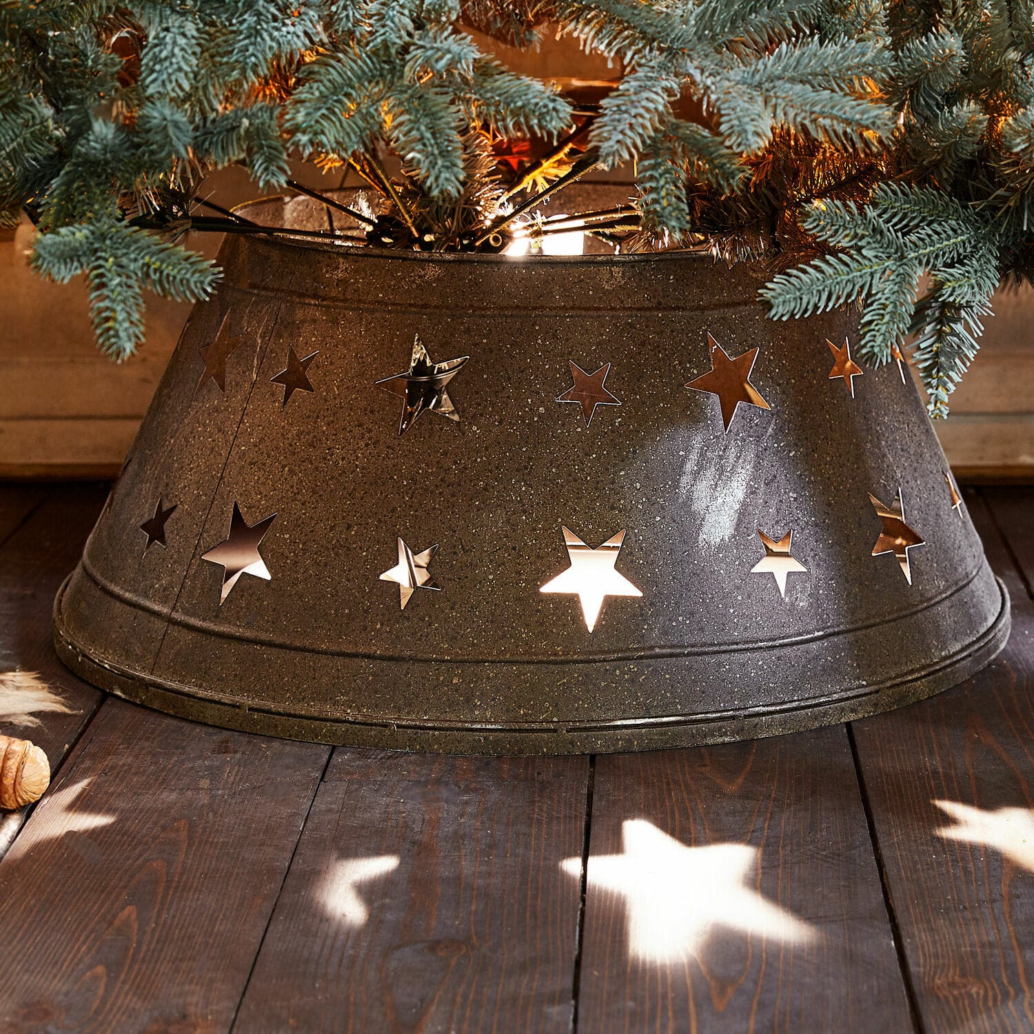 Base para árbol de Navidad Ysabelle Base metálica para árbol de Navidad con recortes de estrellas en gris oscuro, decoración navideña sobre suelo de madera