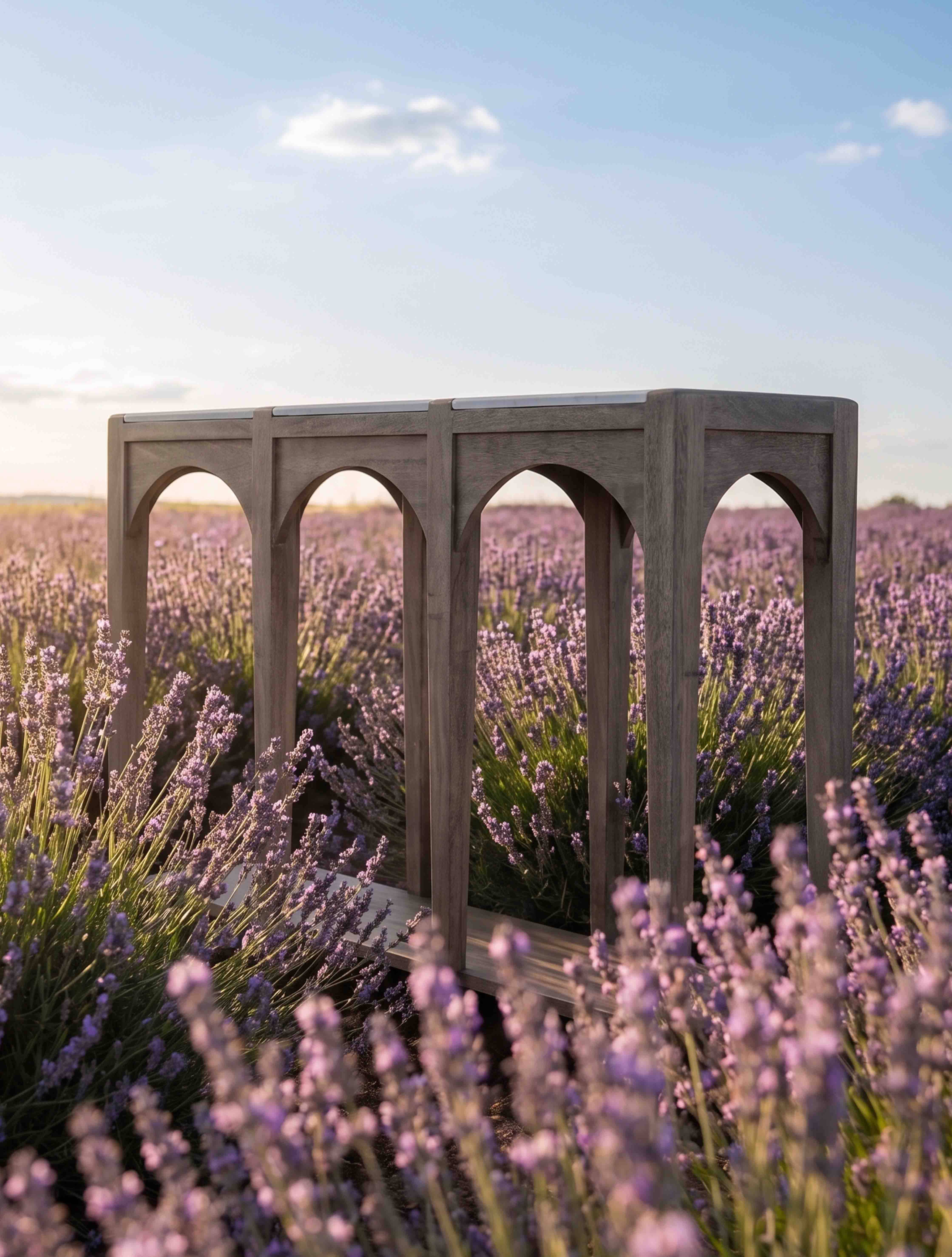 Mesa de jardín de madera gris con patas arqueadas sobre un campo de lavanda morada