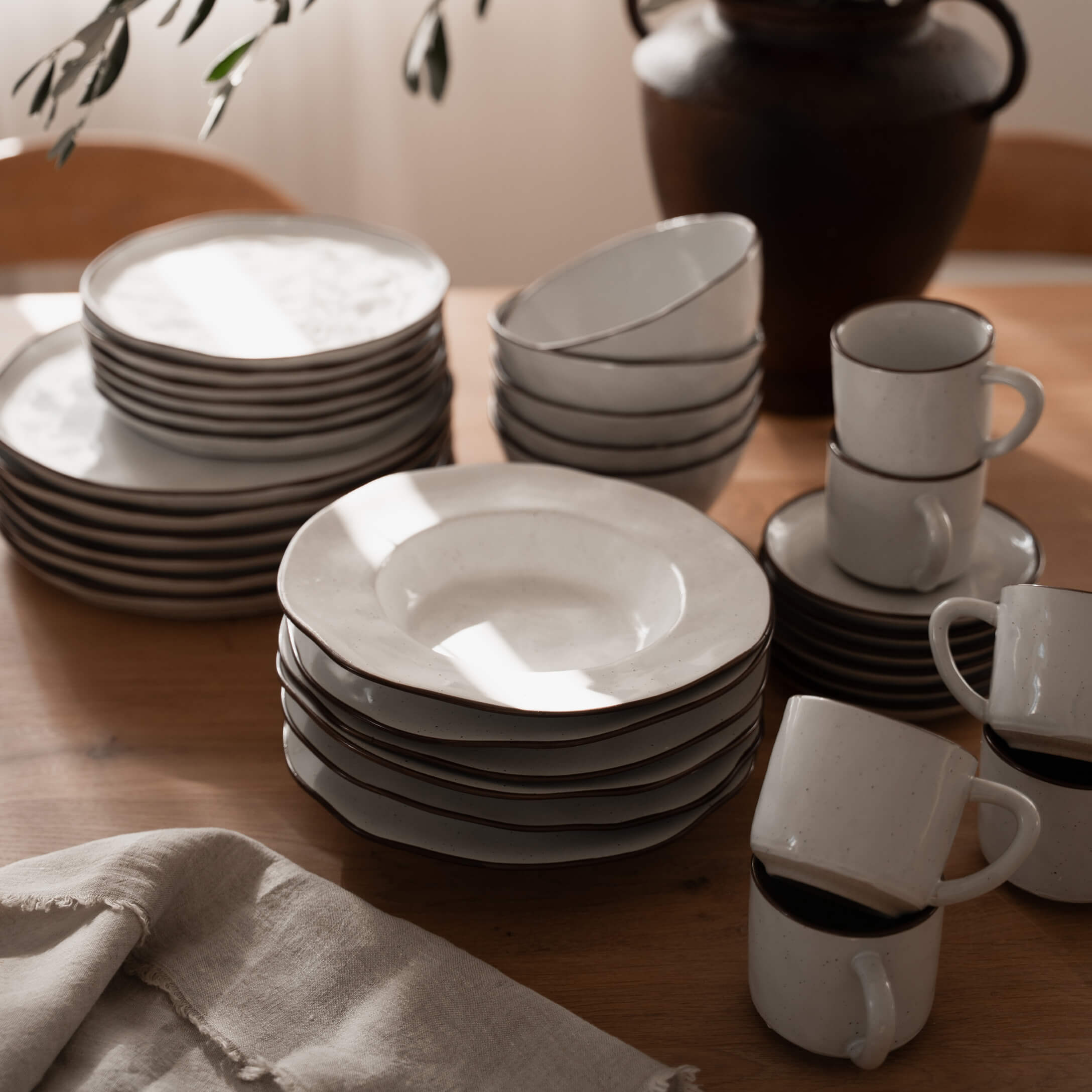 Juego de vajilla de cerámica blanca con borde marrón sobre mesa de madera, utensilios de cocina
