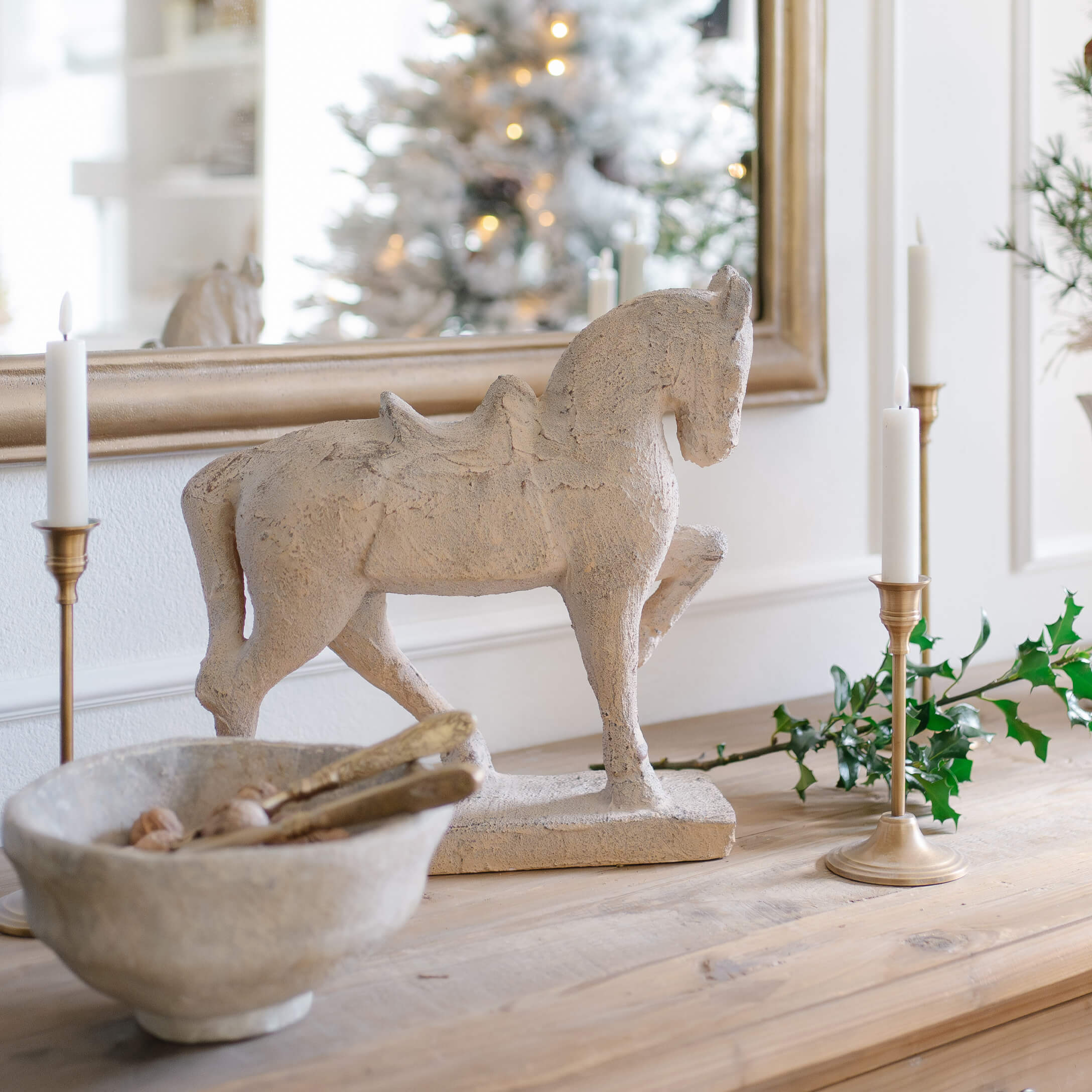 Escultura decorativa de caballo en material tipo piedra beige sobre mesa de madera con velas