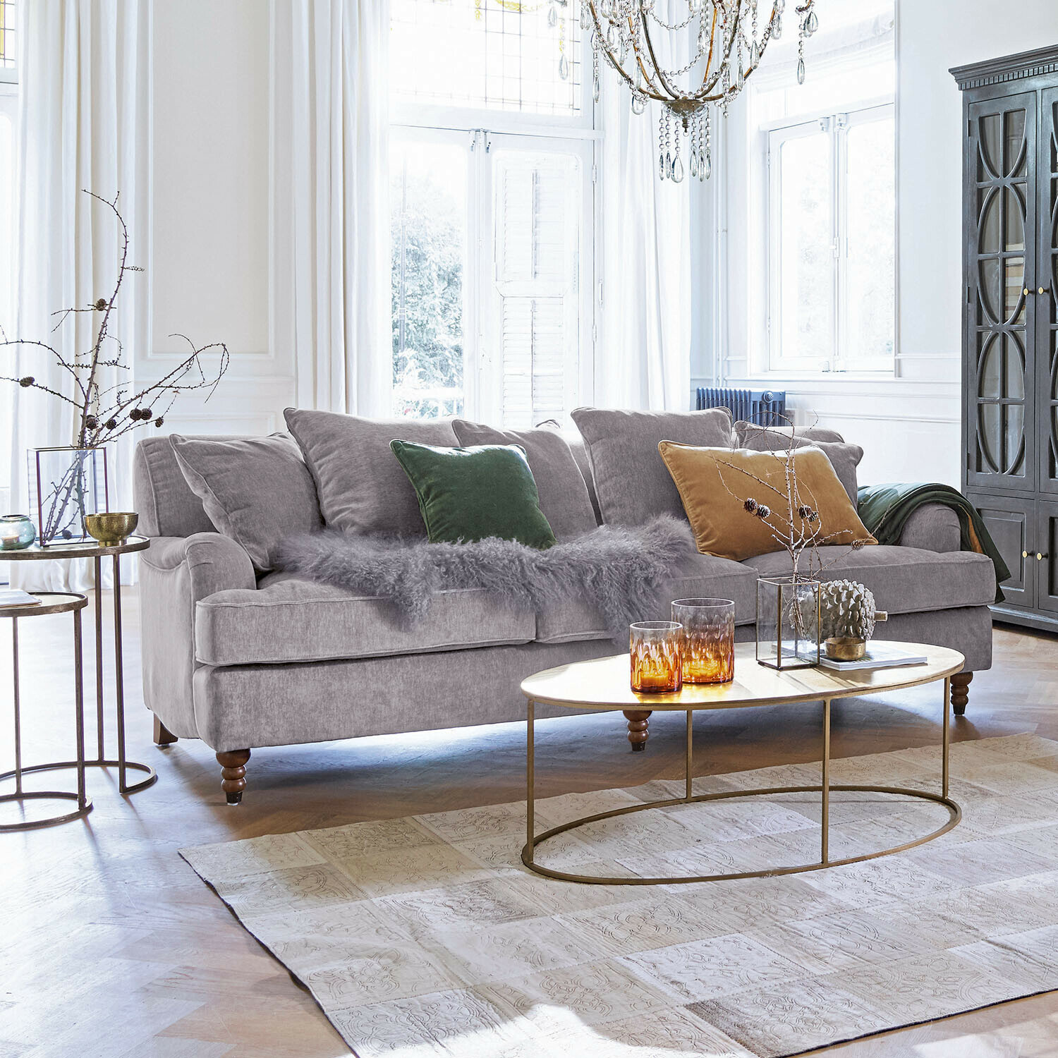 Sofá Isa Sofá gris de tela suave con cojines de colores y mesa de centro ovalada en sala luminosa